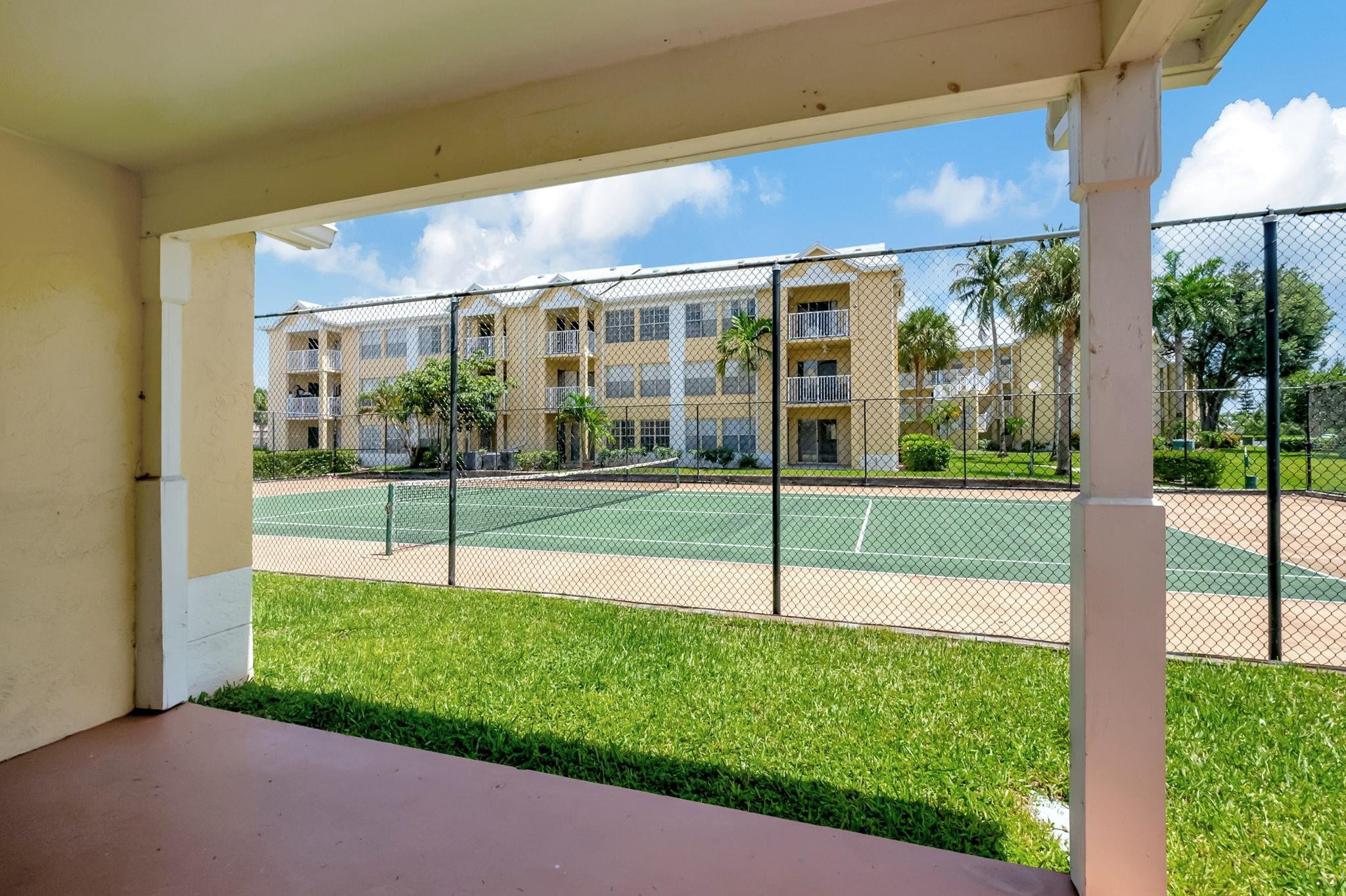 Covered patio overlooks a fenced tennis court and landscaped condominium grounds.