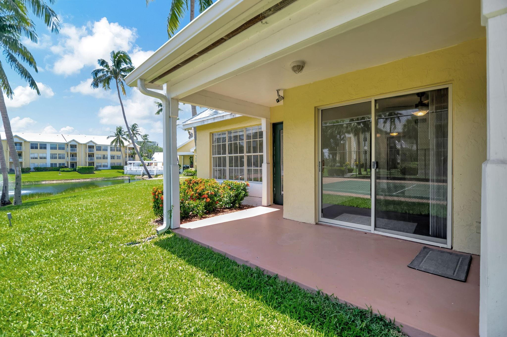 Covered patio with sliding glass doors, flowering shrubs, and a canal-side lawn.