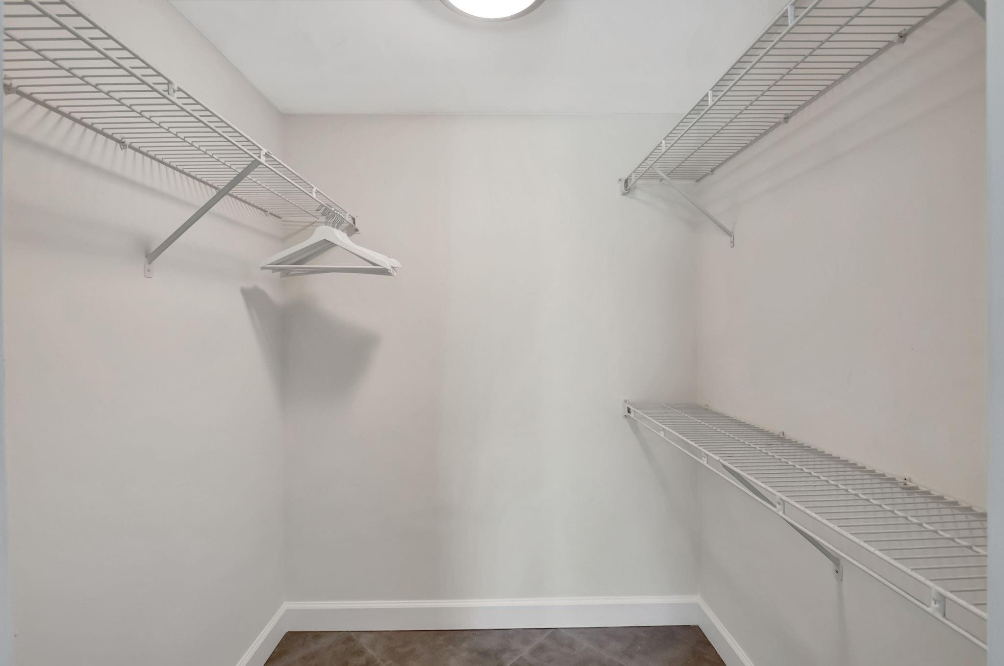 Walk-in closet with white wire shelving, a few hangers, and dark tile flooring.
