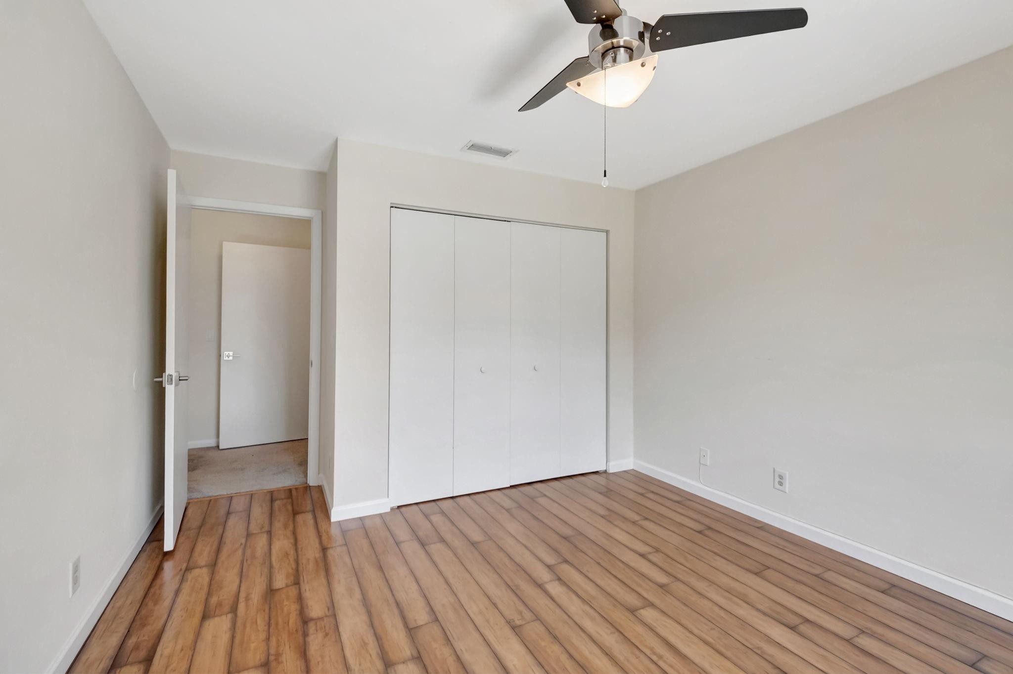 Empty bedroom with wood-look floors, a wide white closet, and a ceiling fan.