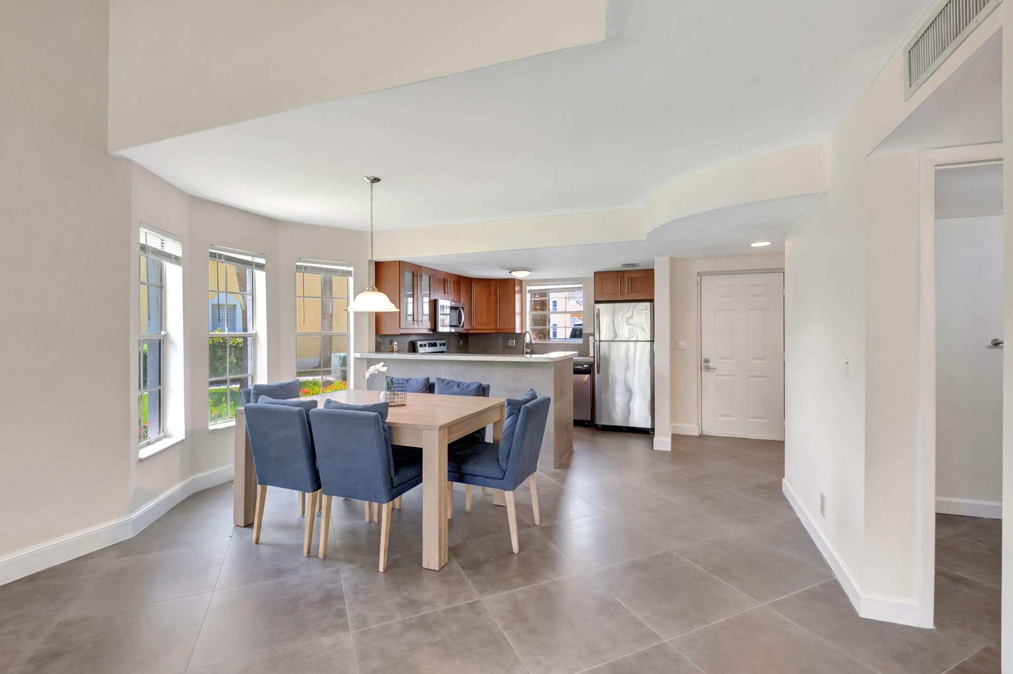 Open dining area with blue chairs, large windows, and a kitchen with wood cabinets and stainless steel appliances.