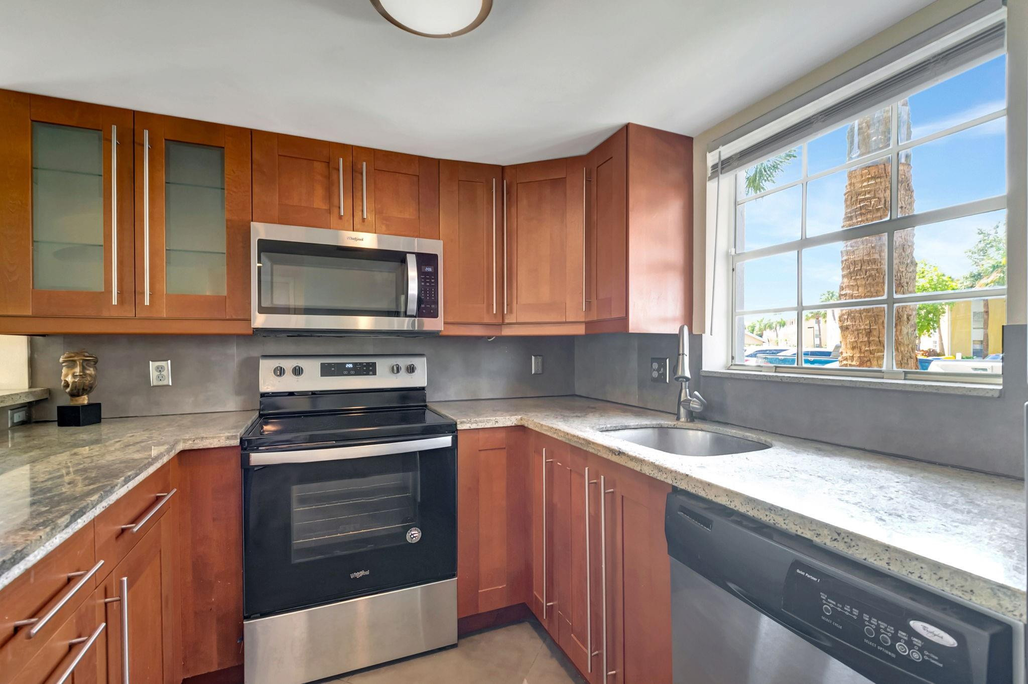 Kitchen with reddish wood cabinets, granite counters, stainless steel appliances, and a large window.