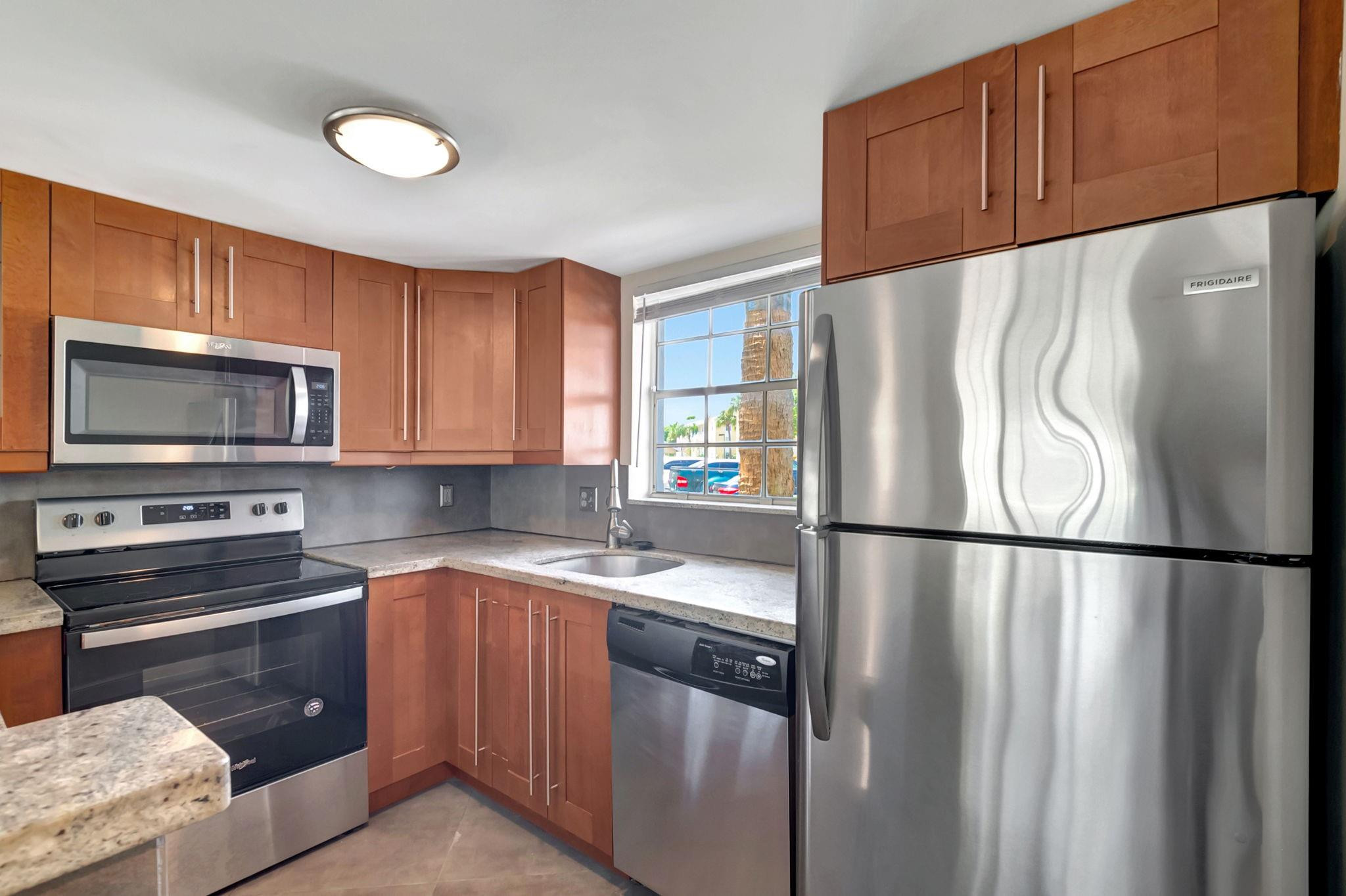 Kitchen with reddish wood cabinets, stone countertops, and stainless steel appliances.