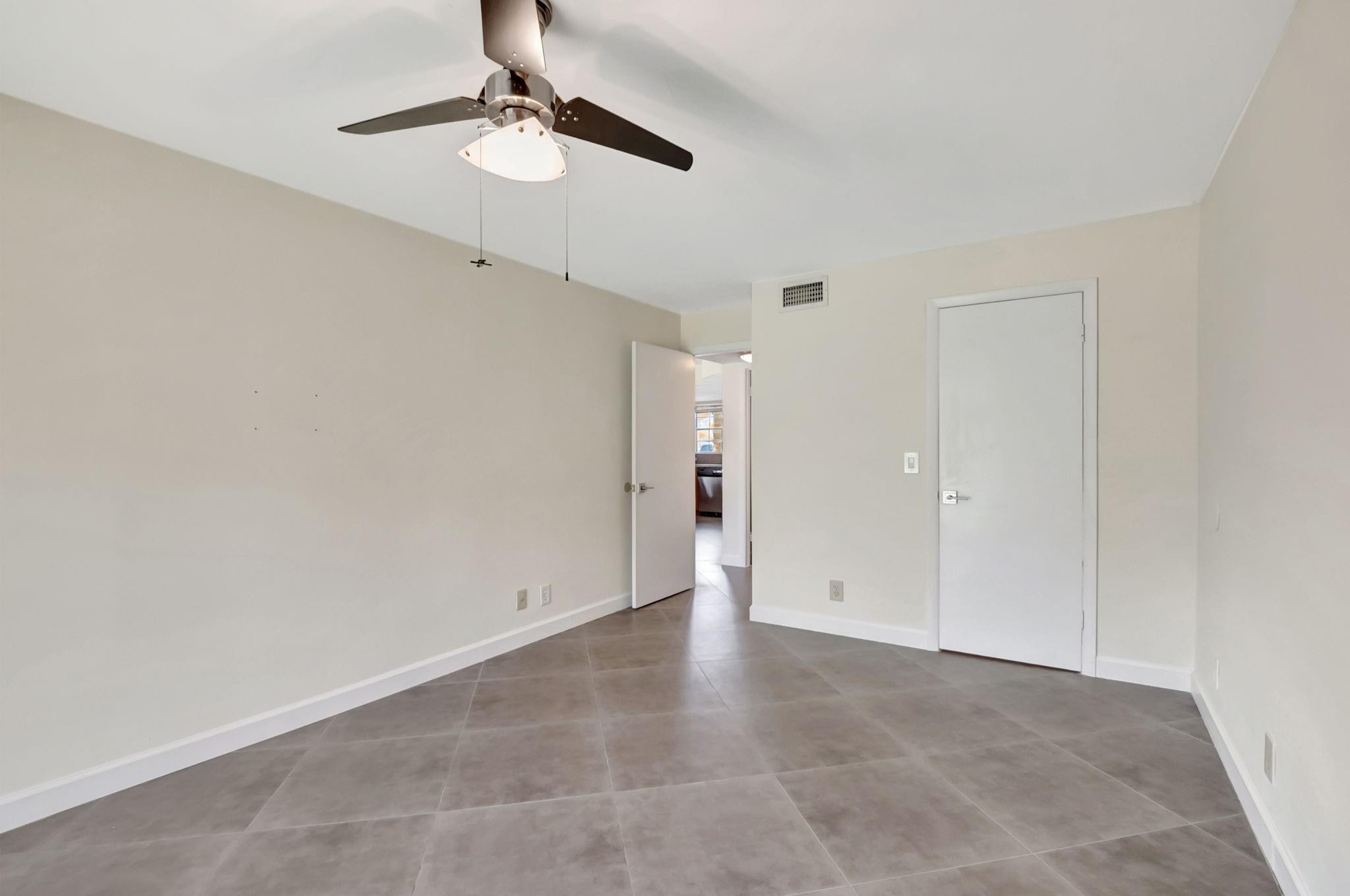 Empty bedroom with gray tile floors, a ceiling fan, and an open doorway.