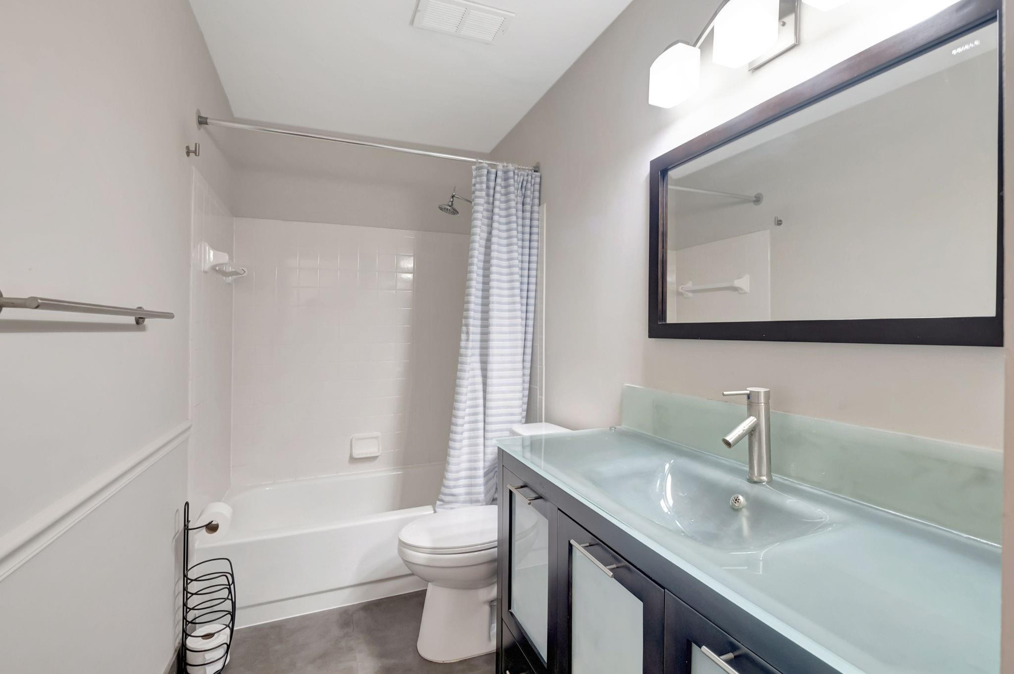 Bathroom with a striped shower curtain and a pale aqua glass sink on a dark vanity.