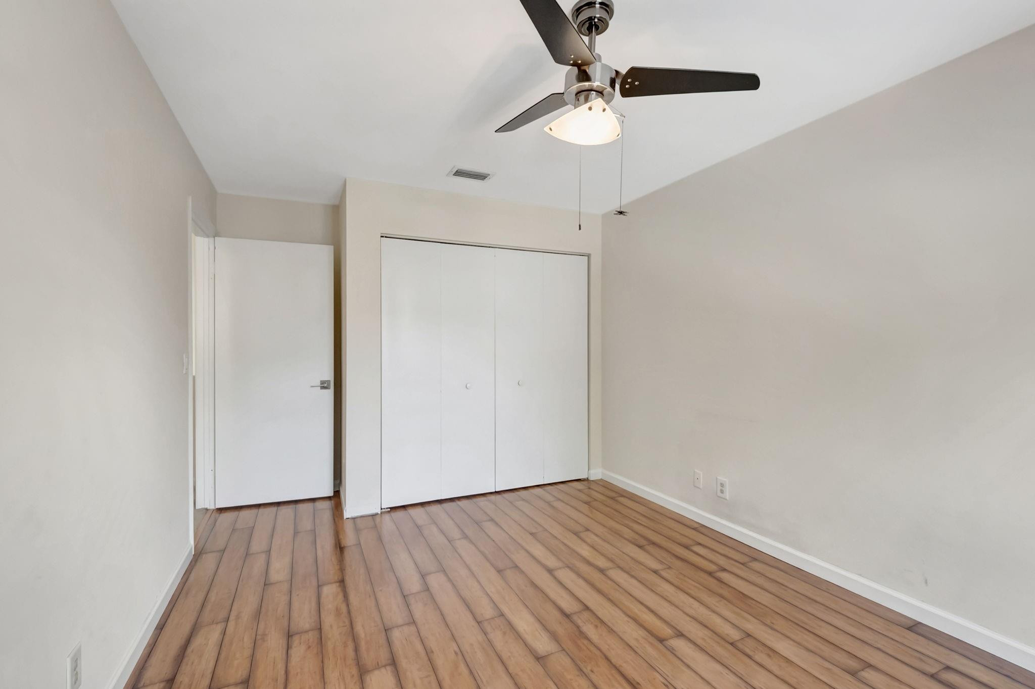 Empty bedroom with wood-look flooring, a white closet, and a ceiling fan with light.