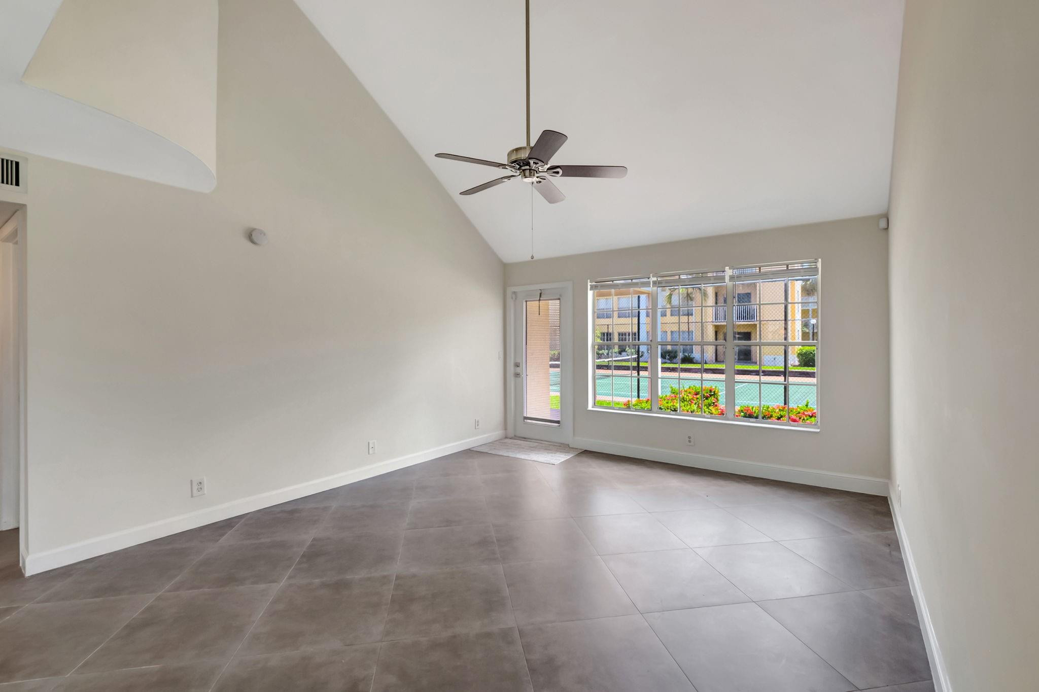 Unfurnished living room with vaulted ceiling, tiled floors, and a large window overlooking a pool.