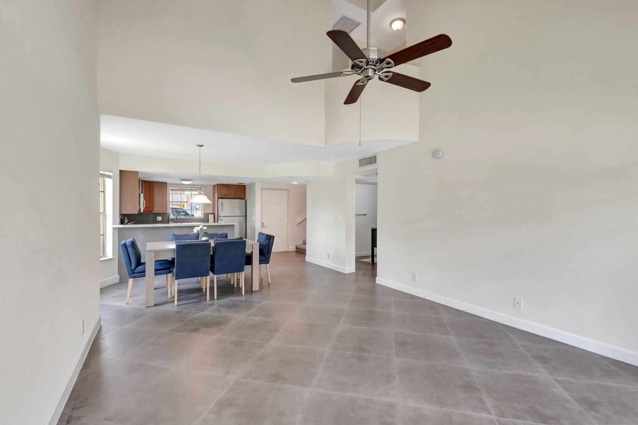 Open-plan dining area with blue chairs, gray tile flooring, and a high ceiling fan.