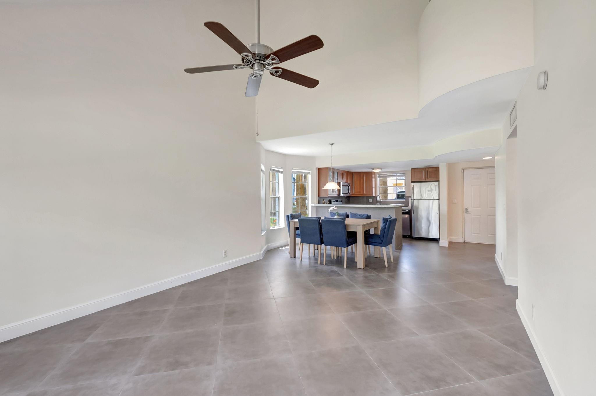 Open dining area with blue chairs, gray tile floors, and a kitchen with wood cabinets and stainless steel appliances.