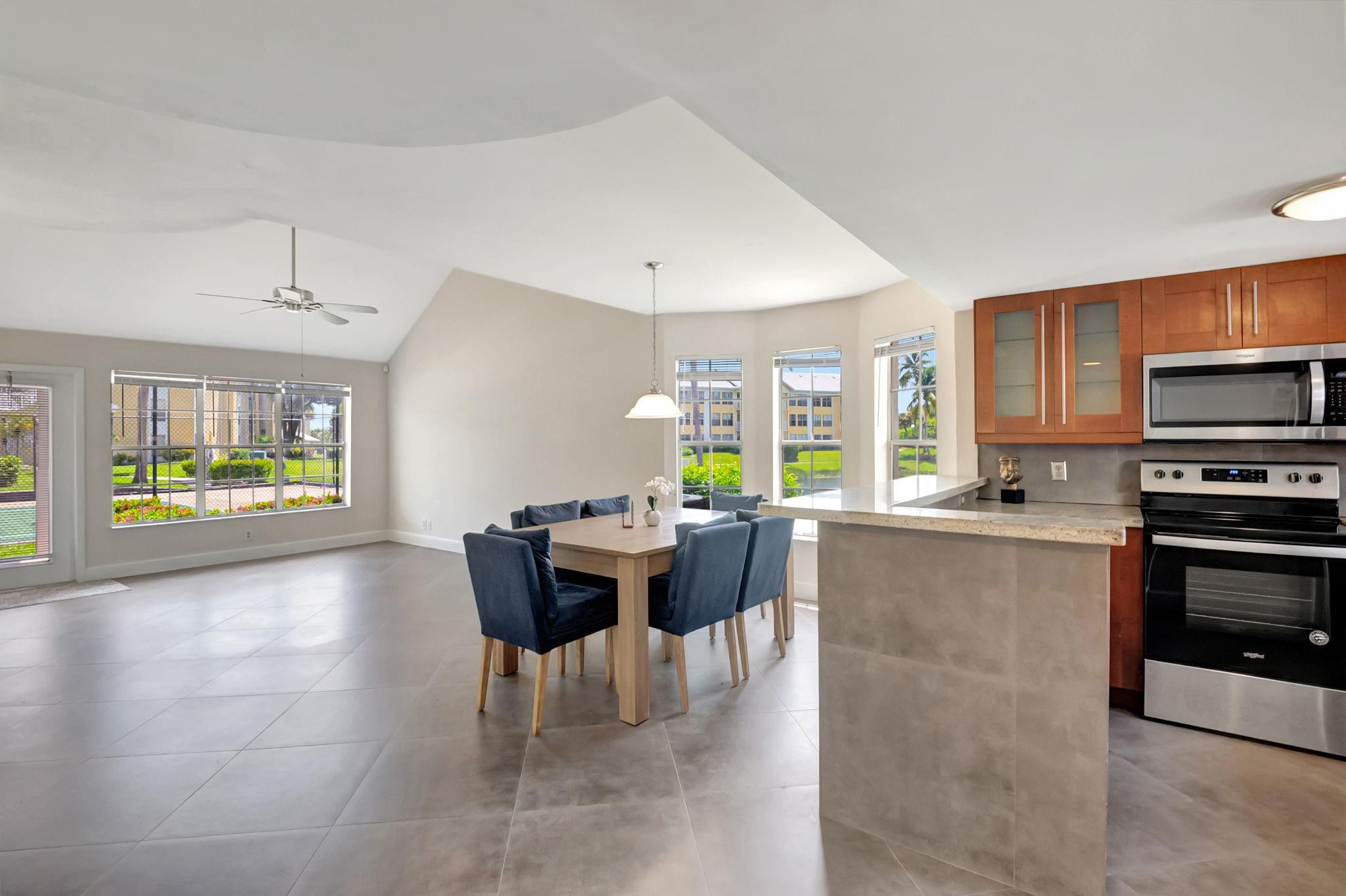 Open kitchen and dining area with warm wood cabinets, a stone breakfast bar, and blue dining chairs.