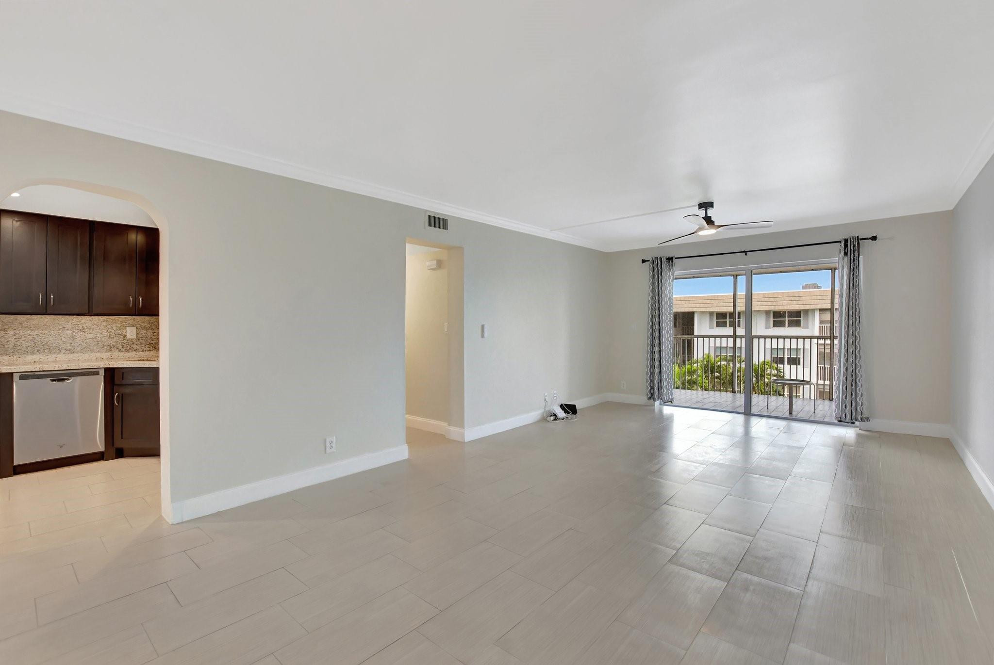 Vacant condo living room with tiled floors, a ceiling fan, and sliding doors to a balcony.