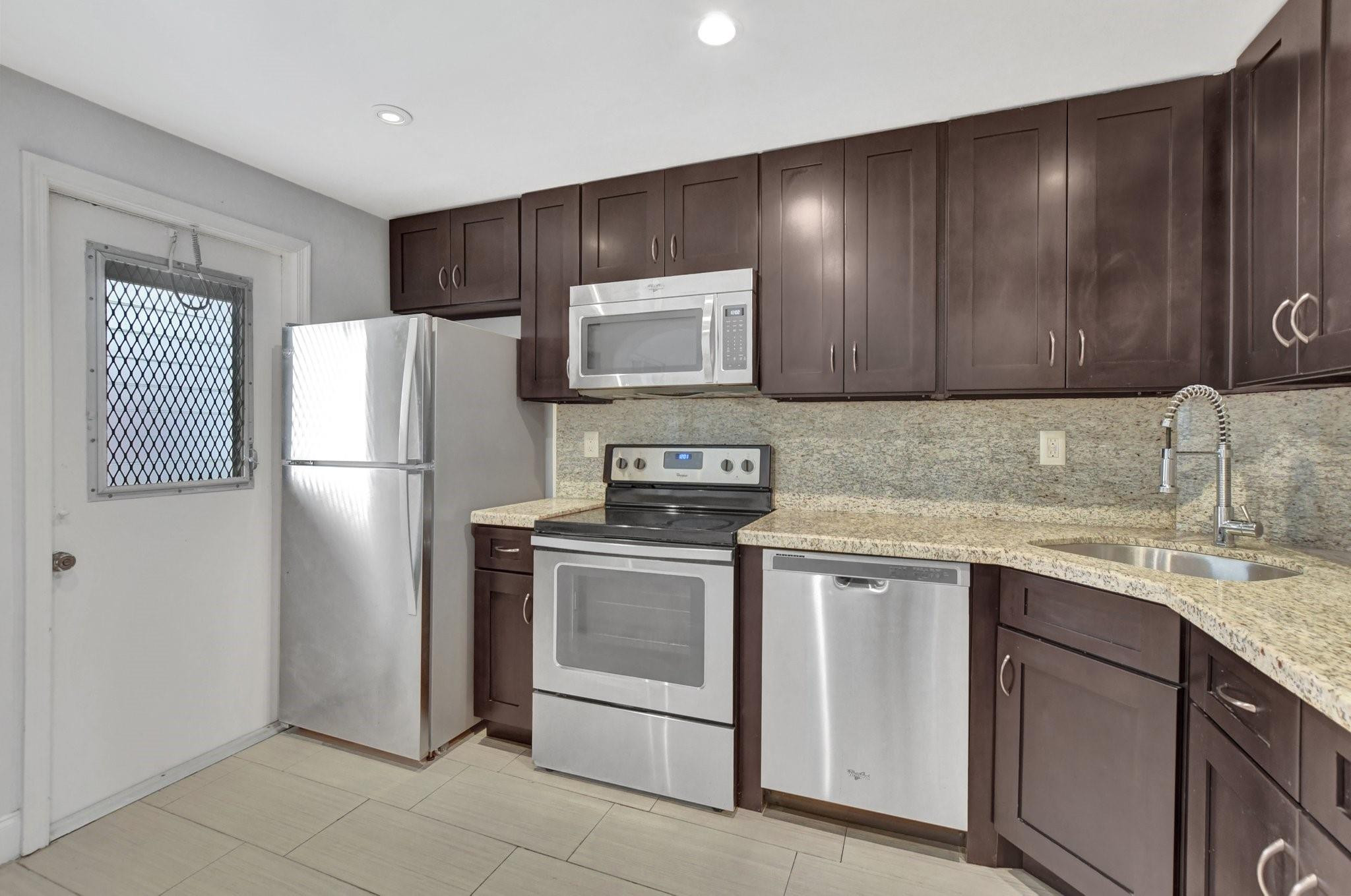 Kitchen with dark wood cabinets, granite counters, stainless steel appliances, and a security-grilled door window.