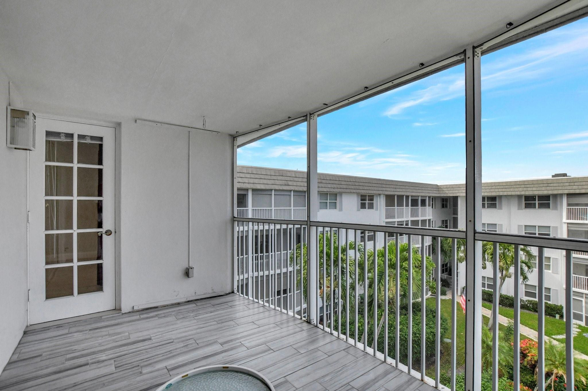 Screened balcony with gray tile flooring overlooking a landscaped courtyard and neighboring condos.