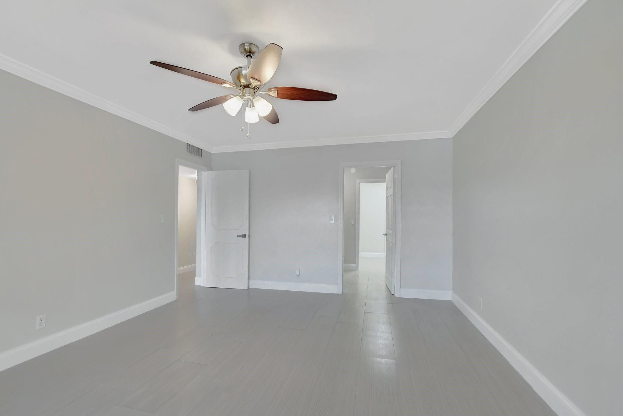 Empty room with pale tile flooring, two open doorways, and a ceiling fan with lights.