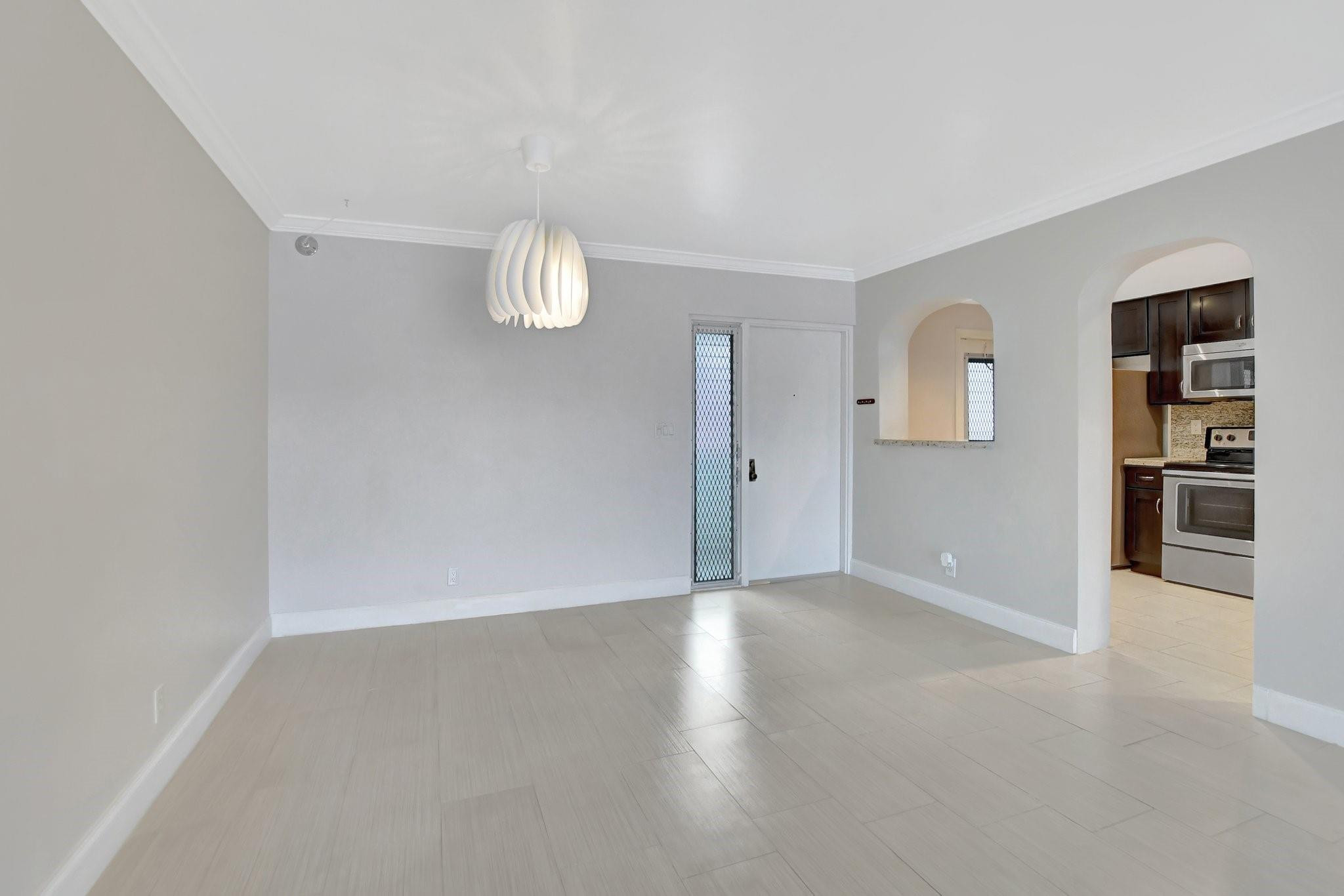 Empty dining area with pale tile floors, a sculptural pendant light, and an arched opening to the kitchen.