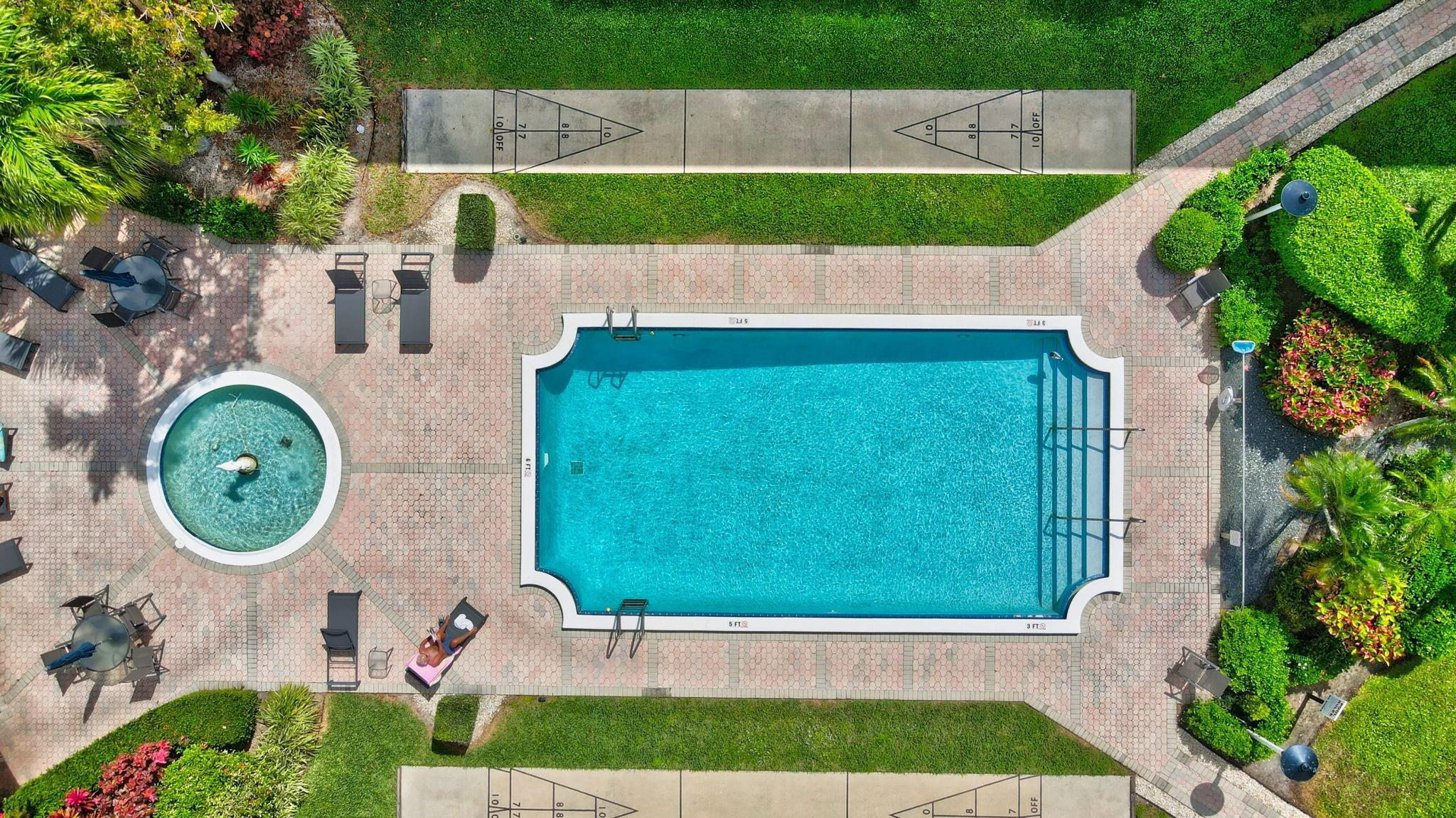Aerial view of a swimming pool and circular spa beside landscaped patio and shuffleboard courts.