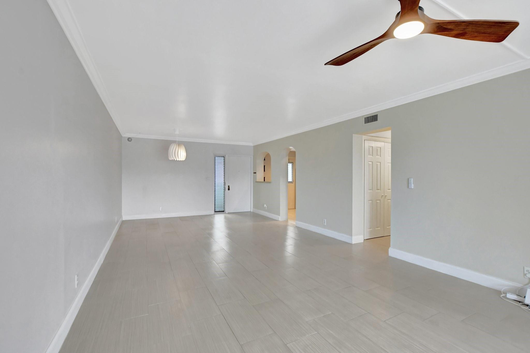 Vacant living room with tiled floors, arched openings, and a wood ceiling fan.
