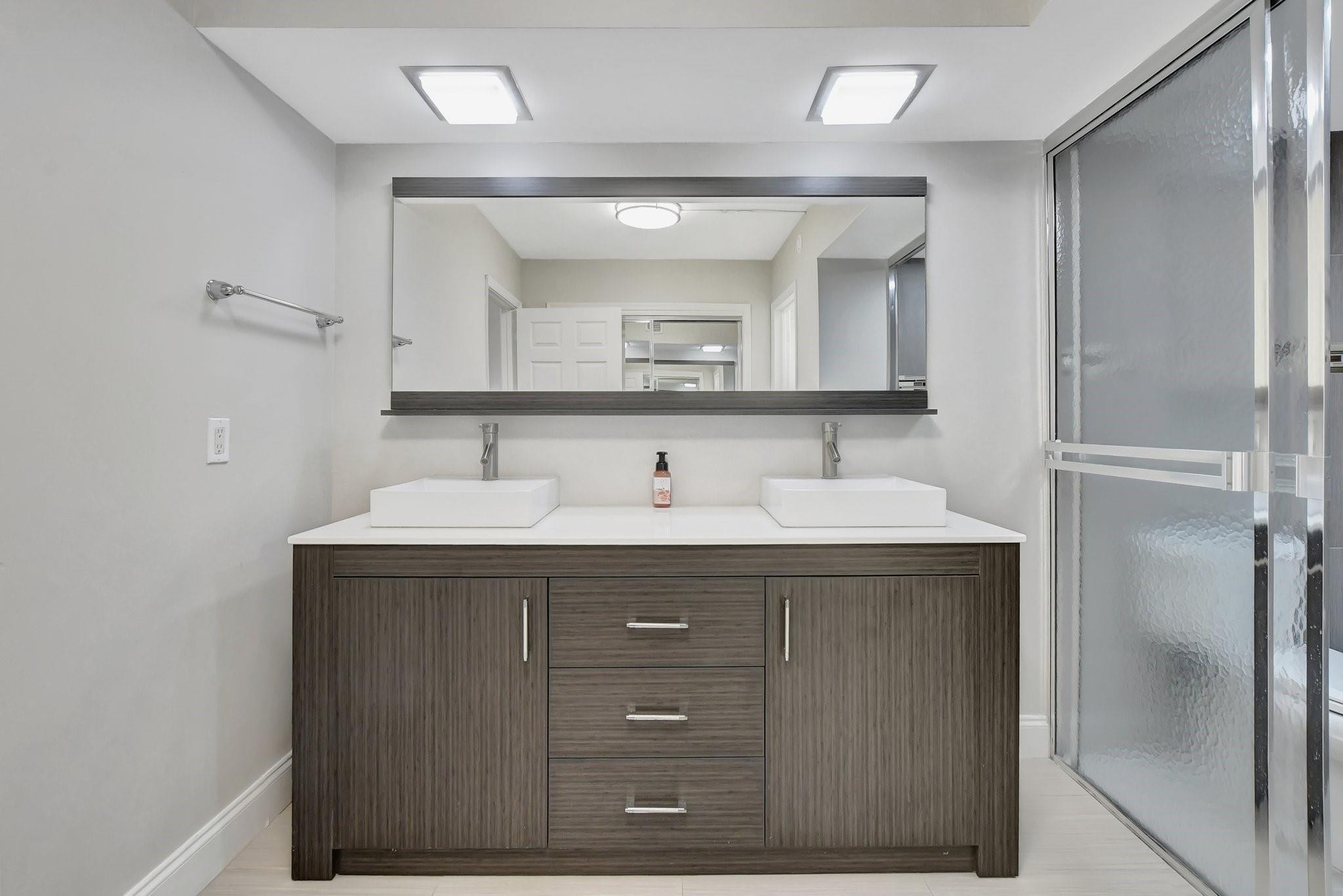 Bathroom with a dark wood double vanity, two vessel sinks, and a frosted-glass shower enclosure.