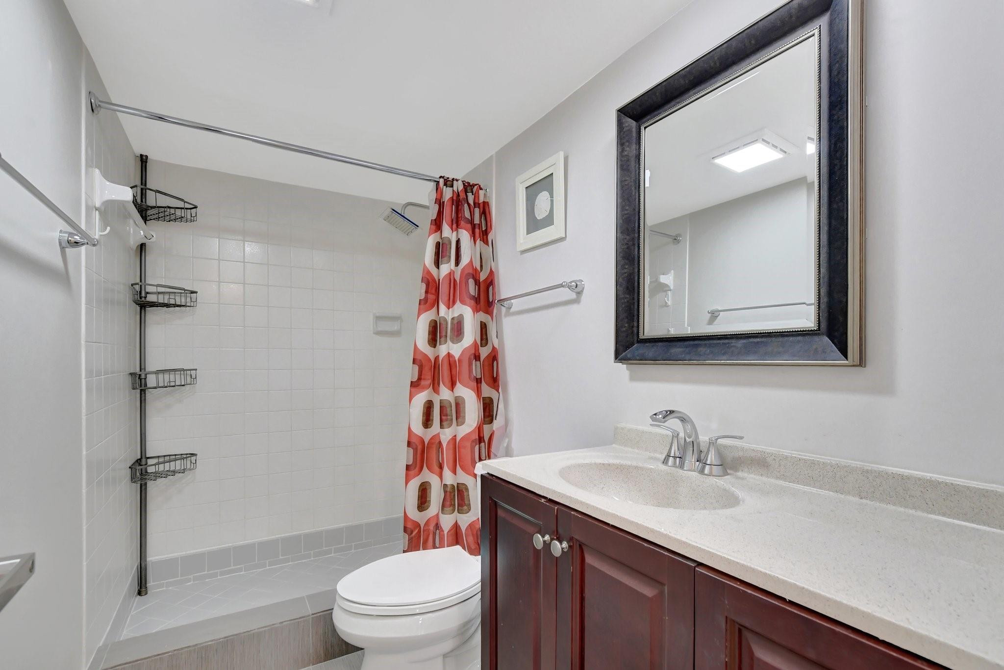 Bathroom with a tiled tub and shower, patterned red curtain, and dark wood vanity.