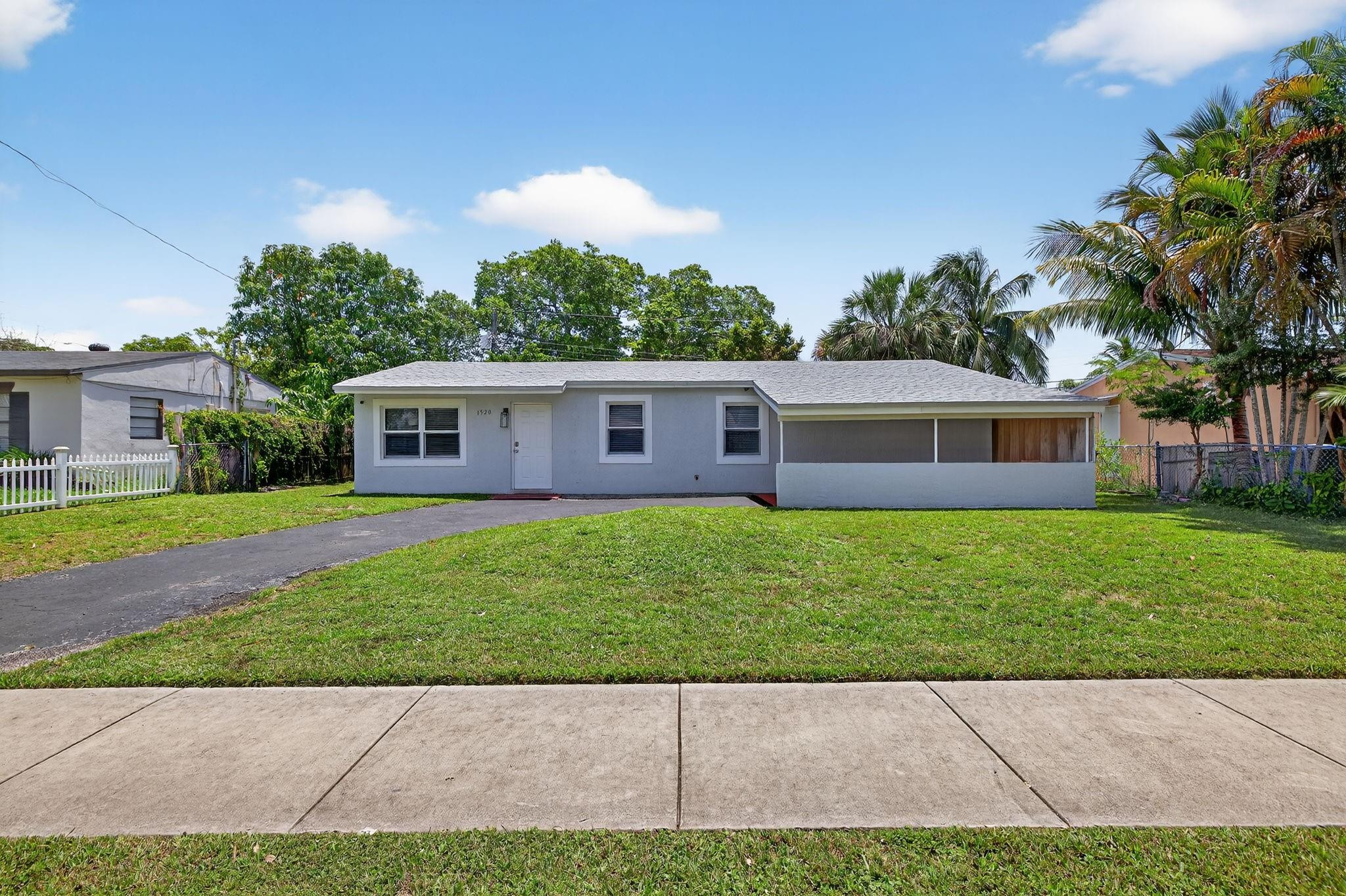 Single-story gray house with a wide driveway, front lawn, and palm trees.