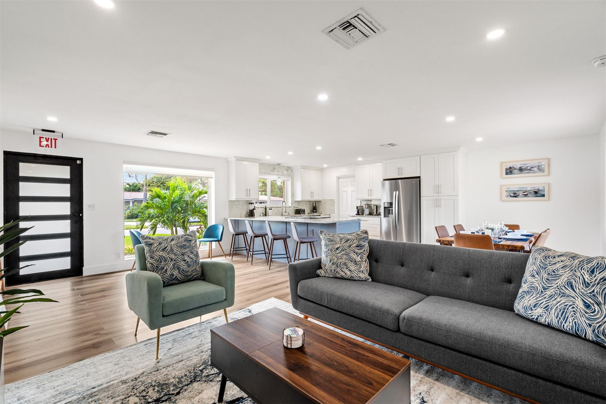 Open-plan living room with gray sofa and green armchair adjoining a white kitchen with blue island.
