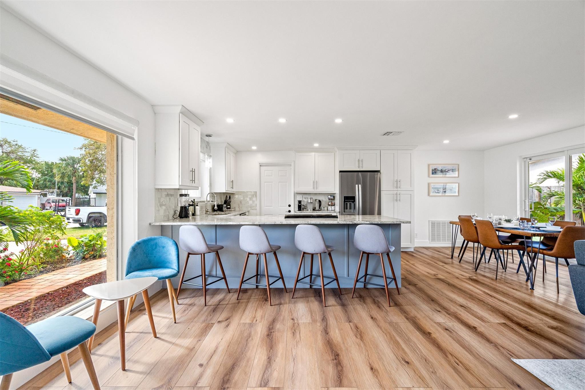 Open kitchen with a blue island and bar stools, adjoining a dining area beside glass doors to the yard.
