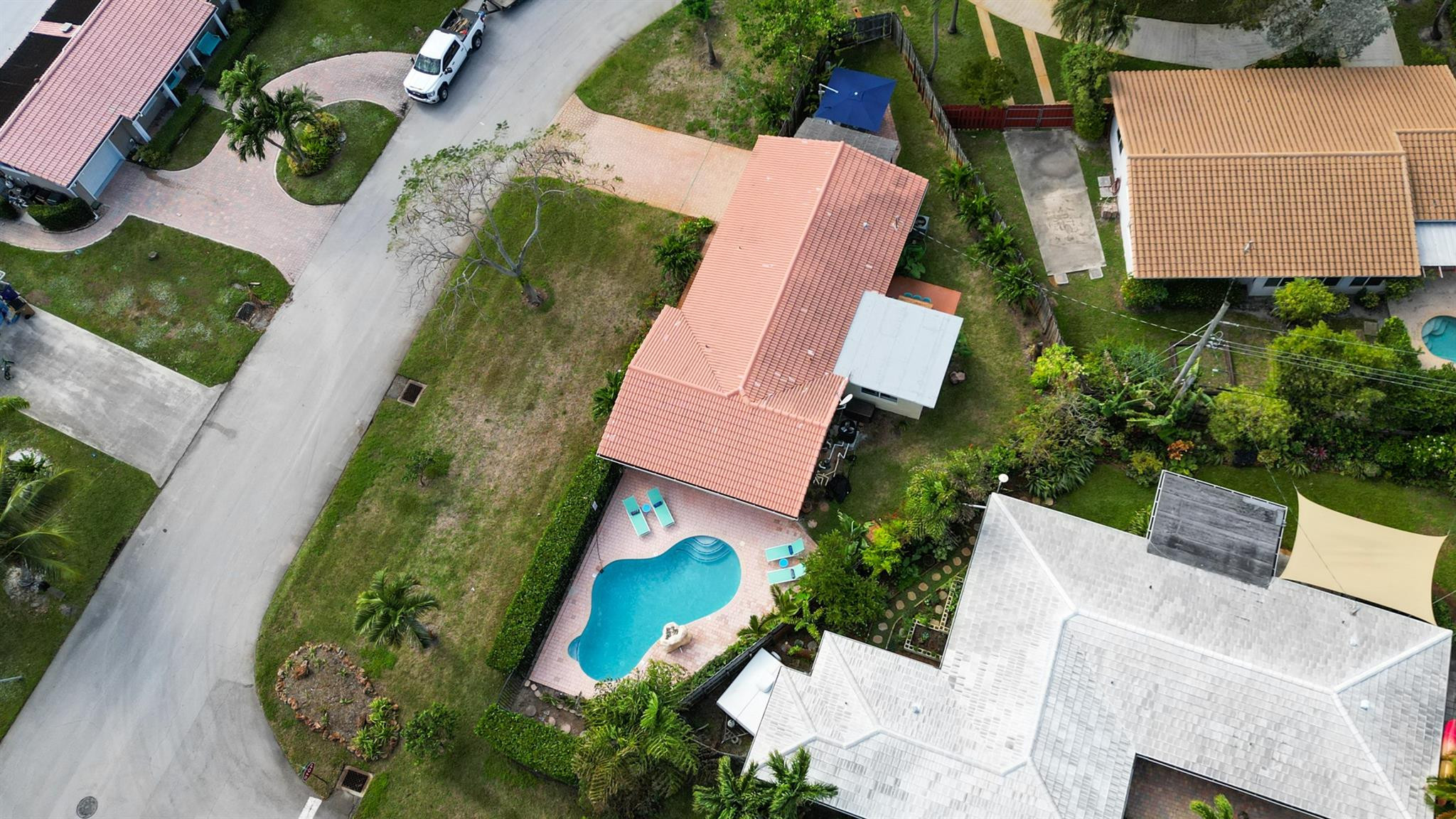 Aerial view of a terracotta-roofed home with a curved pool and landscaped yard.