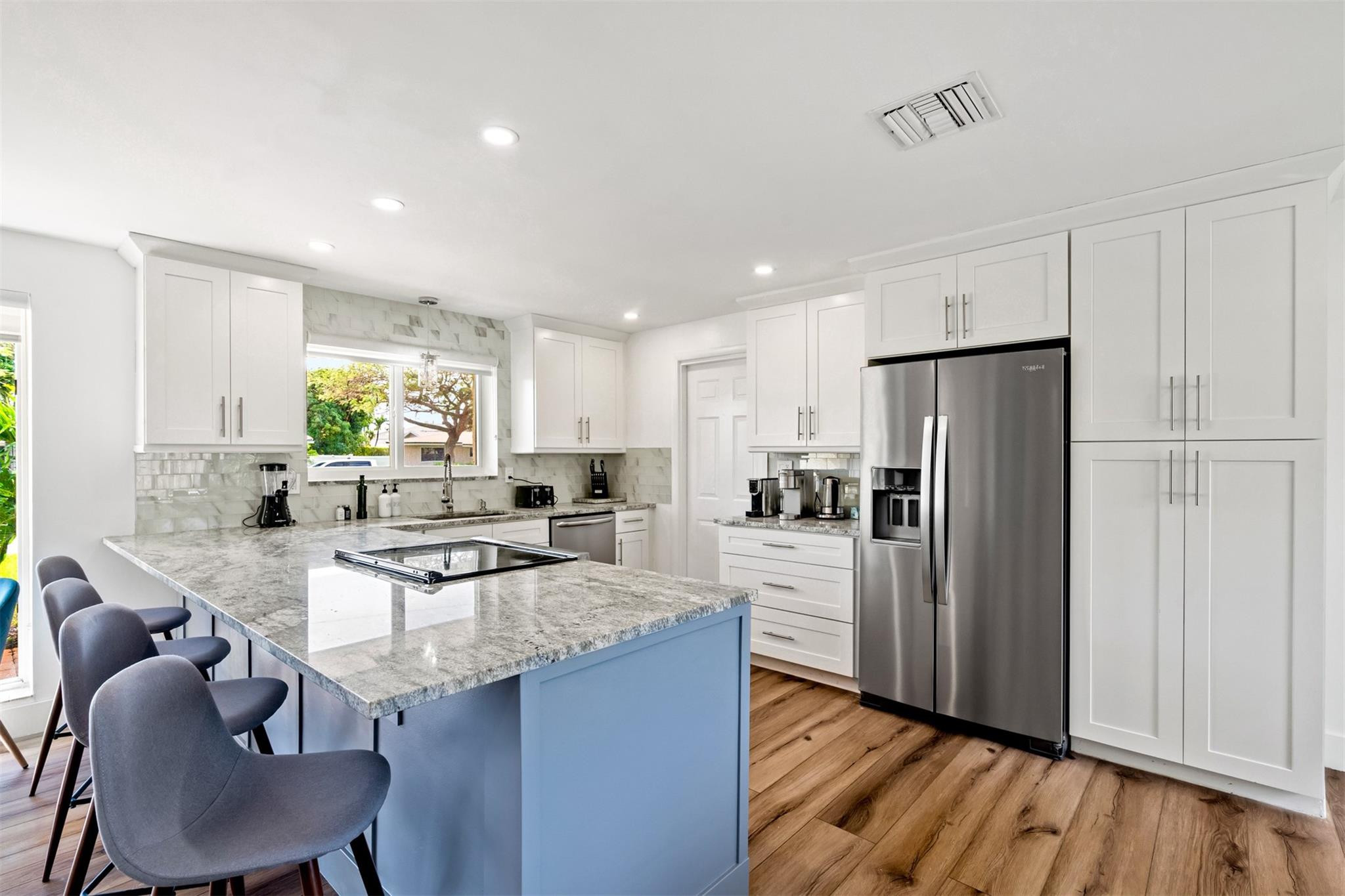 Bright kitchen with a blue island, stone counters, white cabinets, and stainless steel appliances.