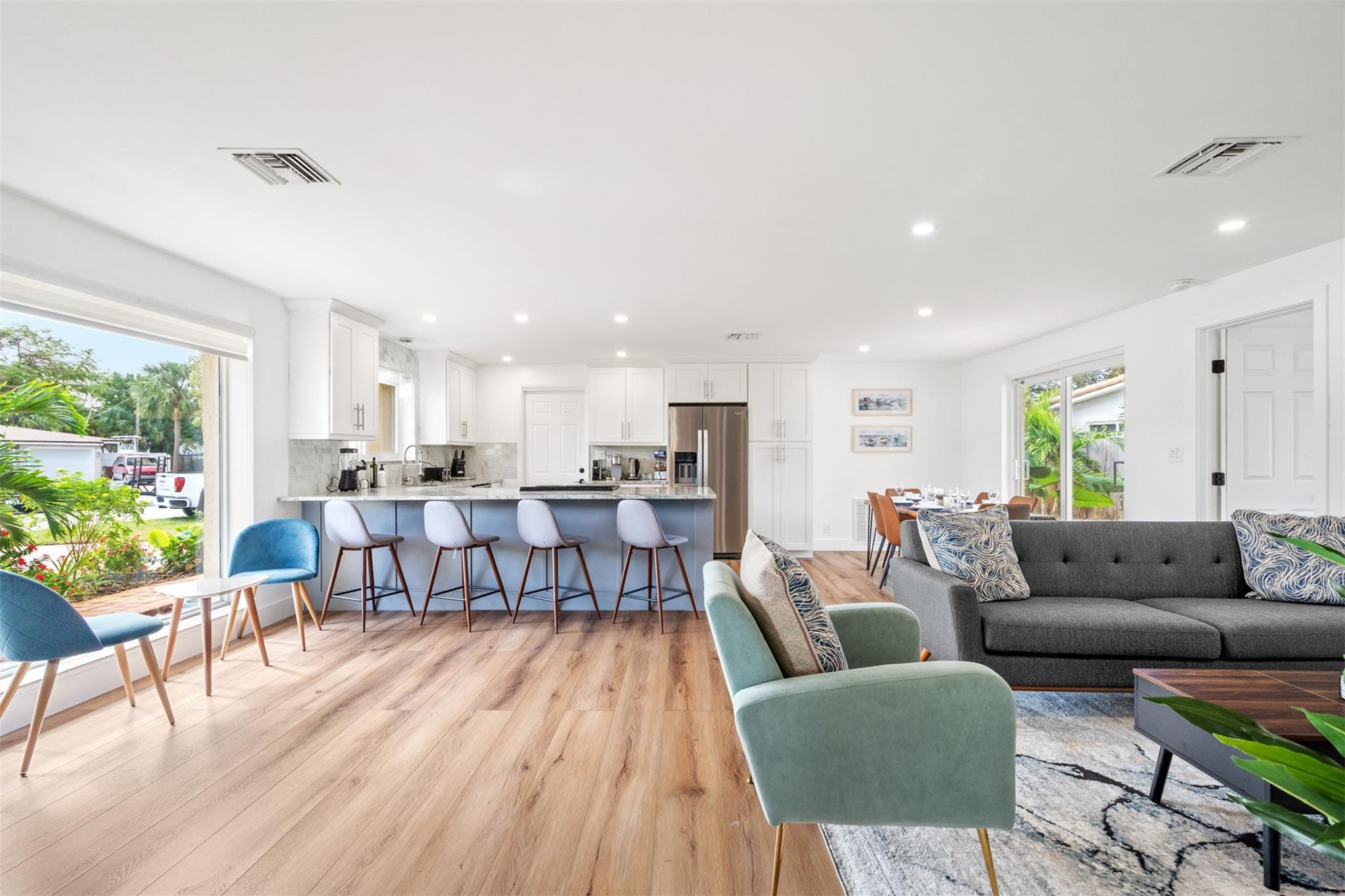 Open-plan kitchen and living room with a blue island, white cabinets, and large windows.