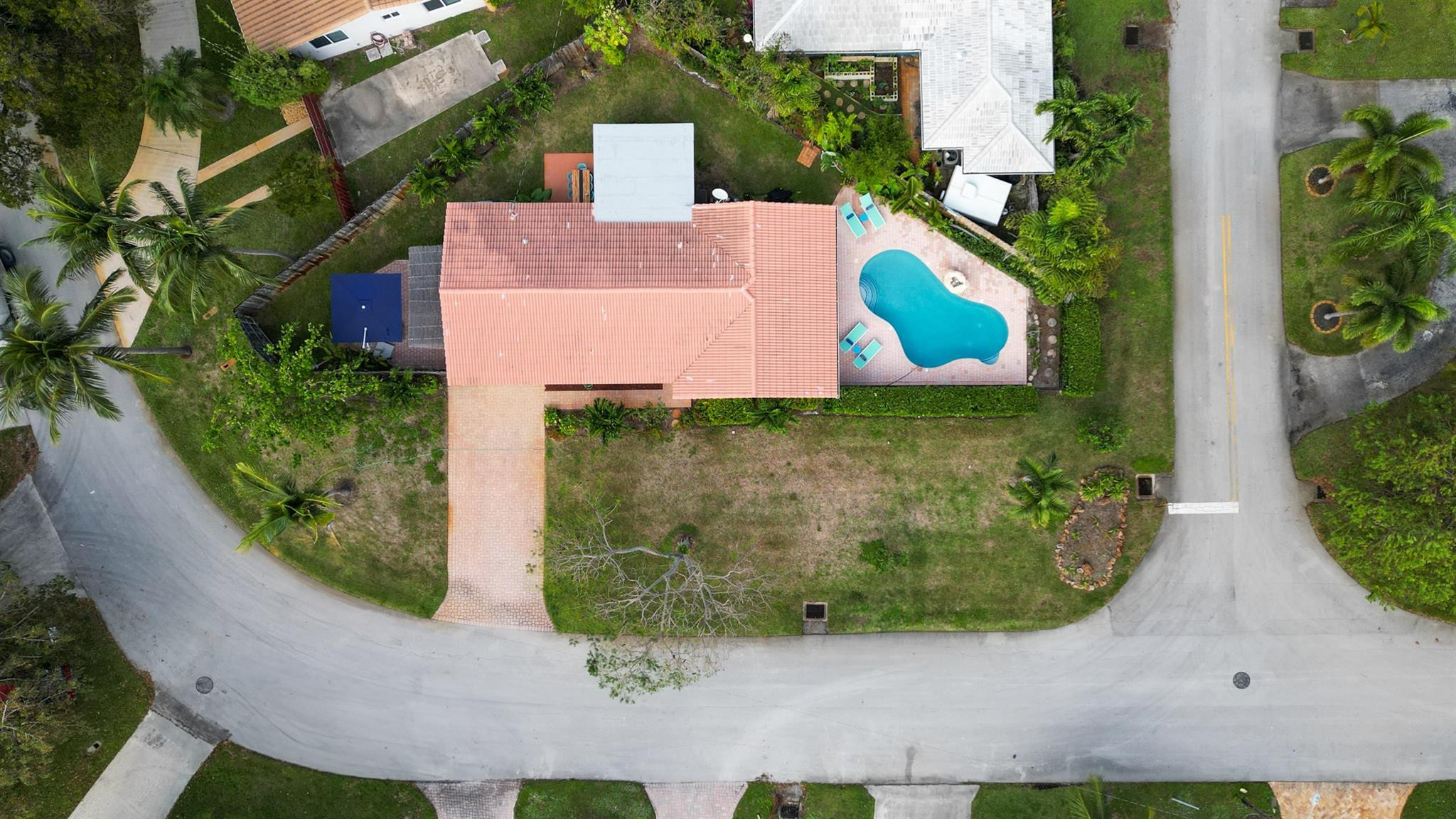 Aerial view of a tile-roofed home with a backyard pool and paved driveway.