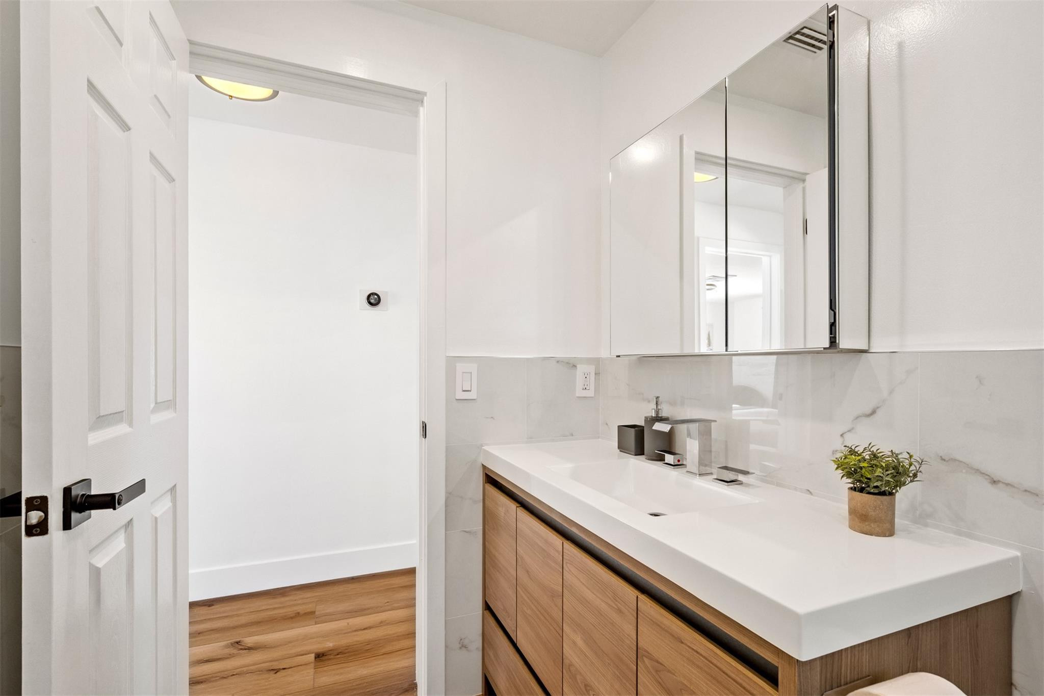 Modern bathroom vanity with wood cabinetry, white countertop, and mirrored medicine cabinet.