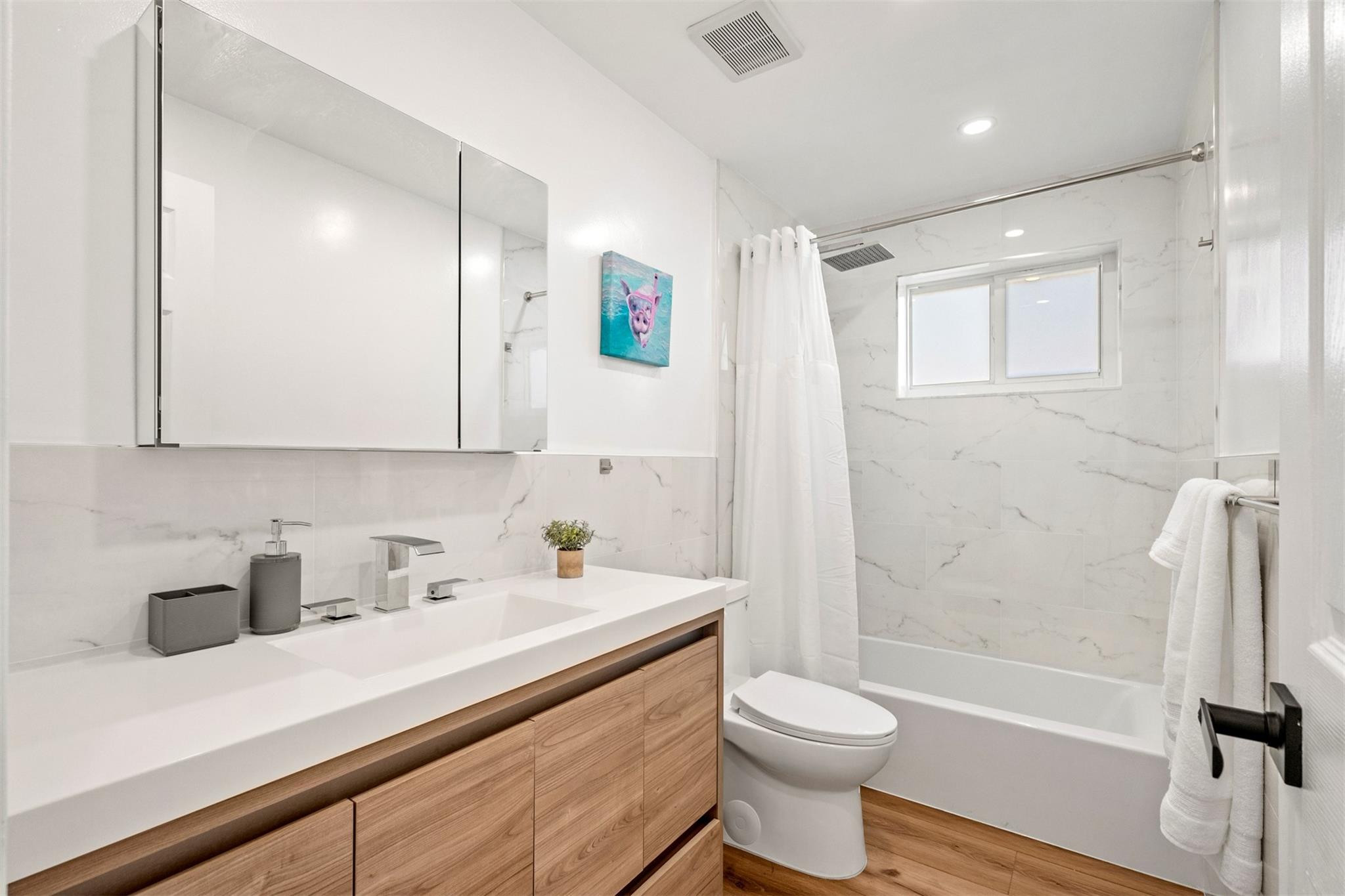 Modern bathroom with a wood-front vanity and marble-look tub-shower surround.