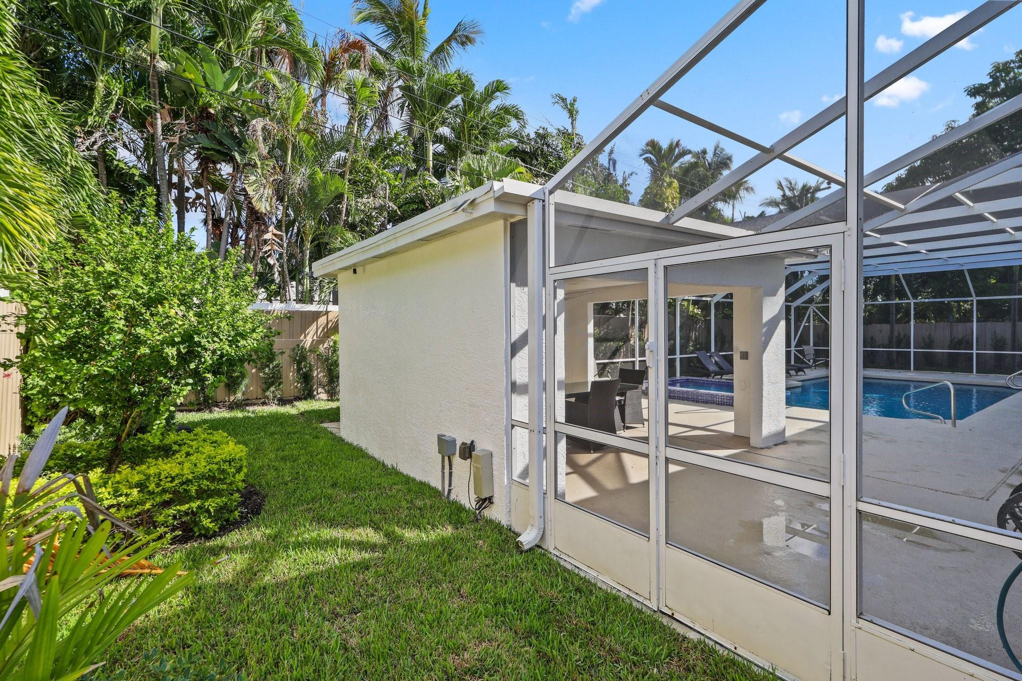 Screened backyard pool and patio beside a white stucco structure, framed by a lawn and tropical landscaping.
