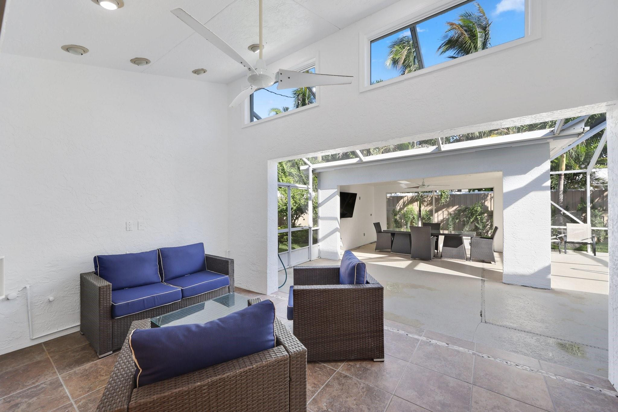 Covered patio with blue-cushioned wicker seating opening to a screened dining area.