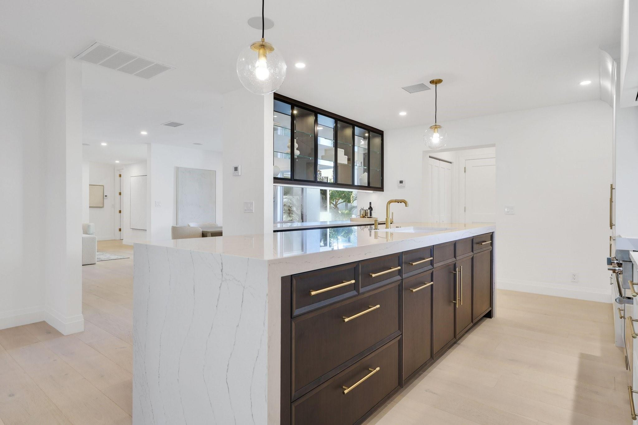 Modern kitchen with a veined stone island, dark cabinetry, brass hardware and glass-front upper cabinets.
