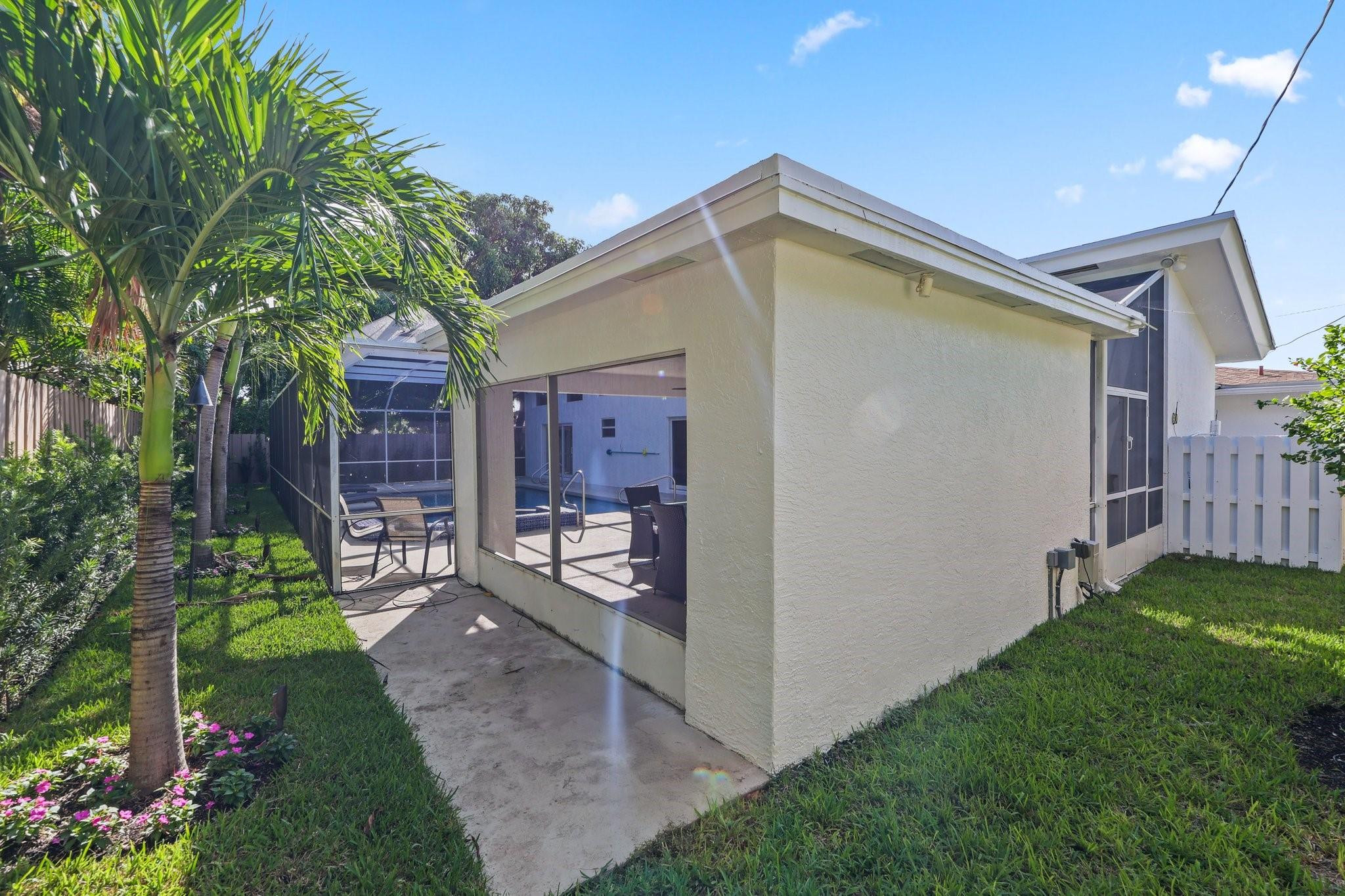 Home’s rear exterior with a screened patio, outdoor seating, lawn, and palm trees.