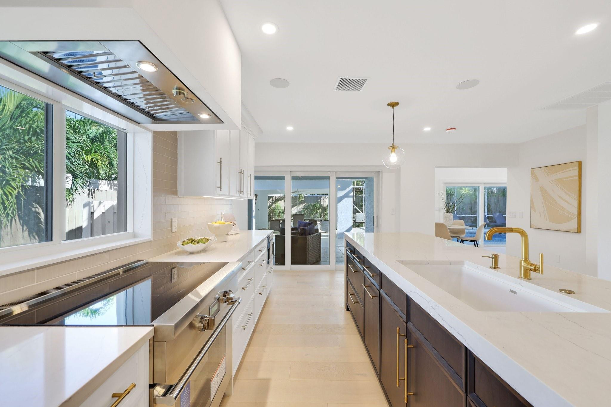 Modern kitchen with a long island, gold fixtures, and sliding doors opening to a patio.