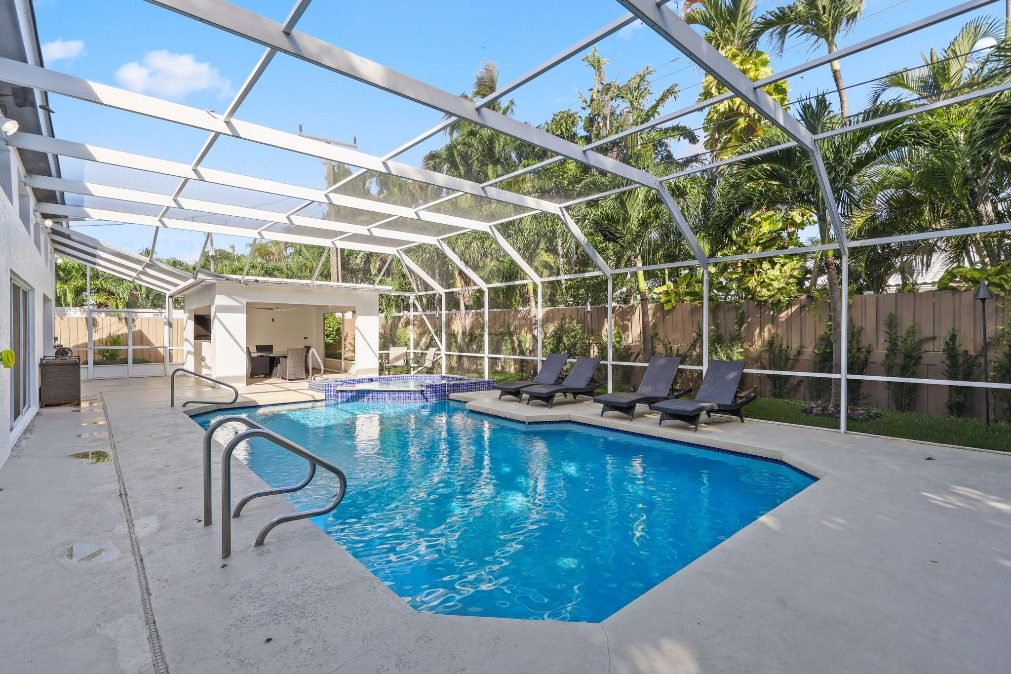 Swimming pool beneath a screened enclosure, with a raised spa and lounge chairs.