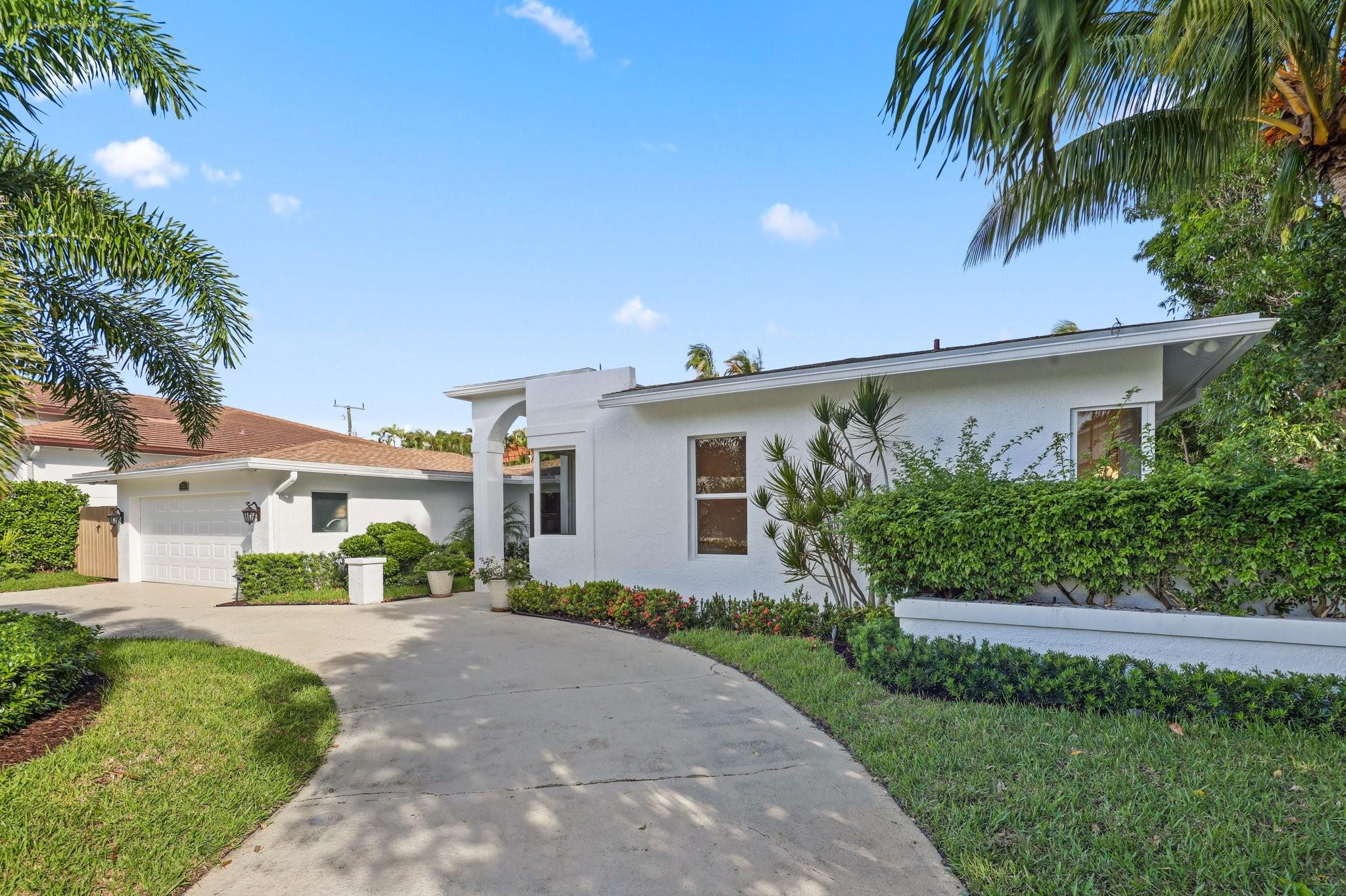 White single-story home with an attached garage, curved driveway, and tropical landscaping.