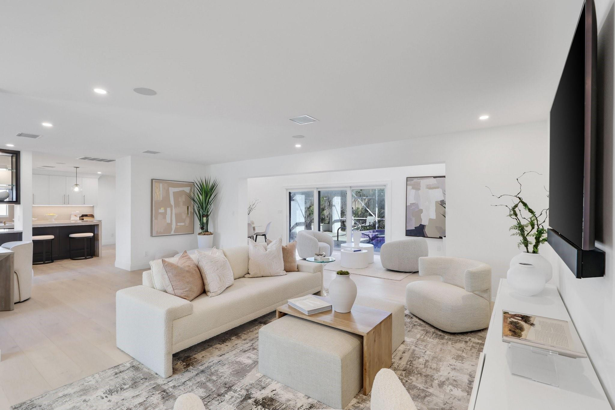 Open-plan living room with cream seating, a wall-mounted TV, and sliding doors to a patio and pool.
