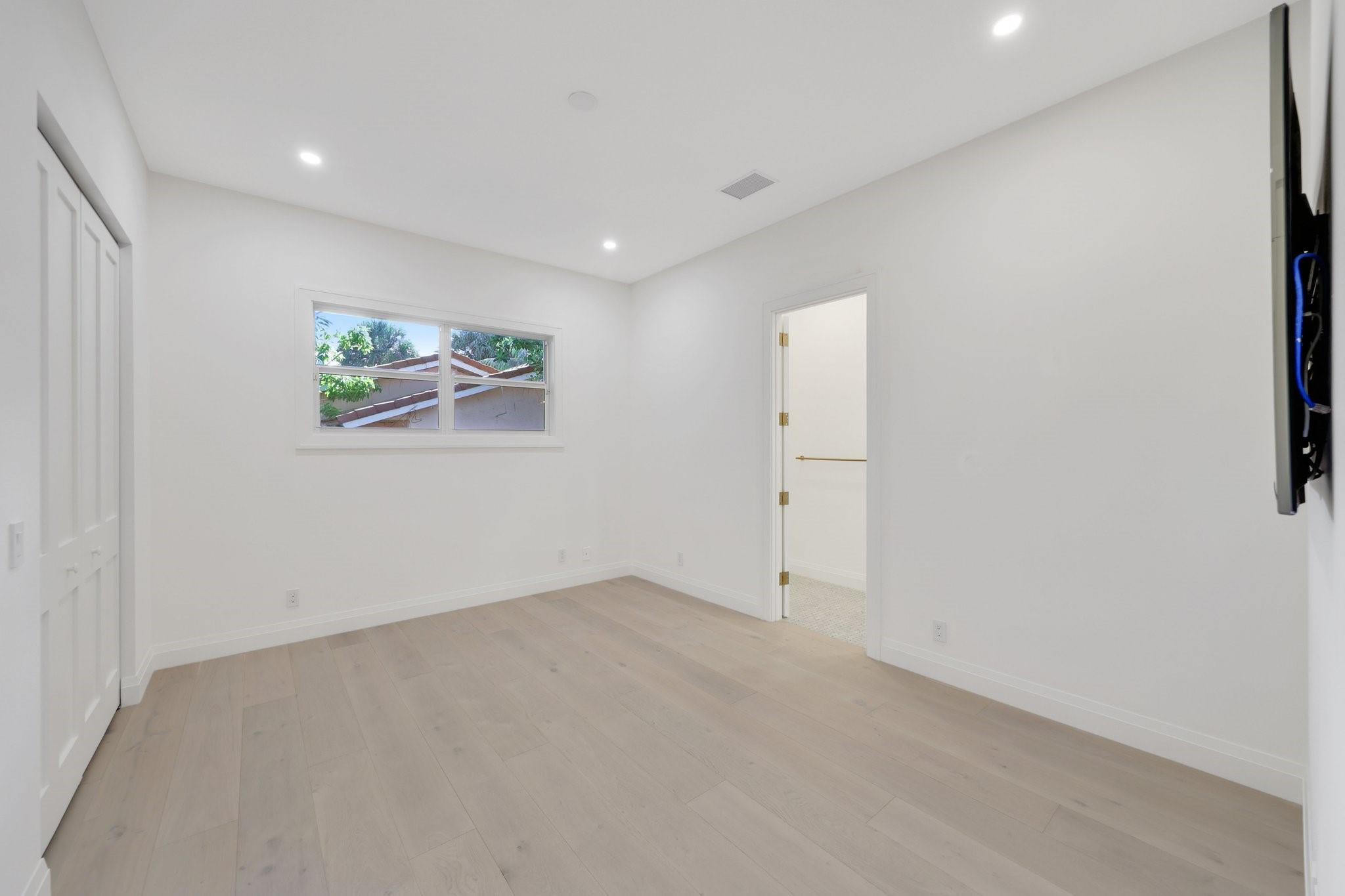 Empty room with pale wood flooring, a small window, and an open doorway to a tiled room.