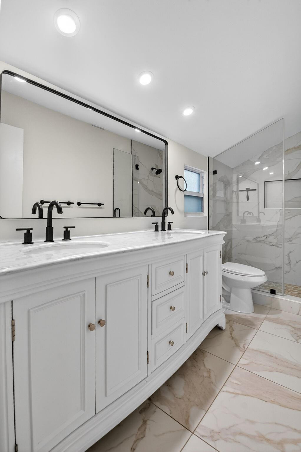 Bathroom with a white double vanity, black faucets, and a glass-enclosed marble-look shower.