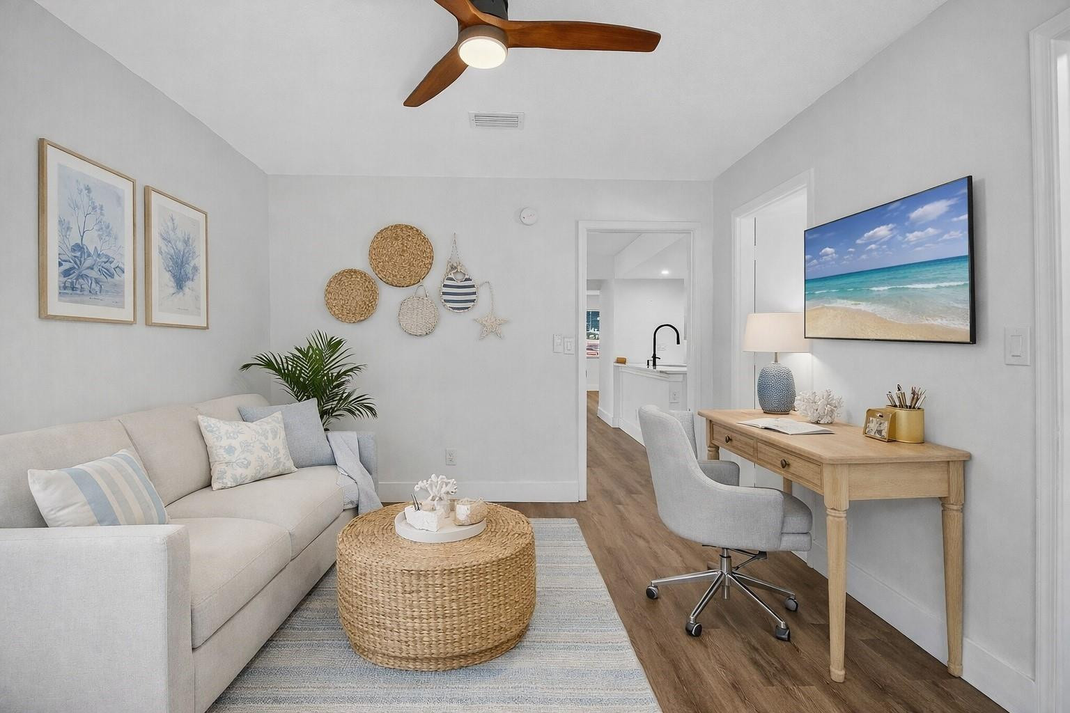 Living room with a light sofa, woven coffee table, and desk beneath a wall-mounted television.