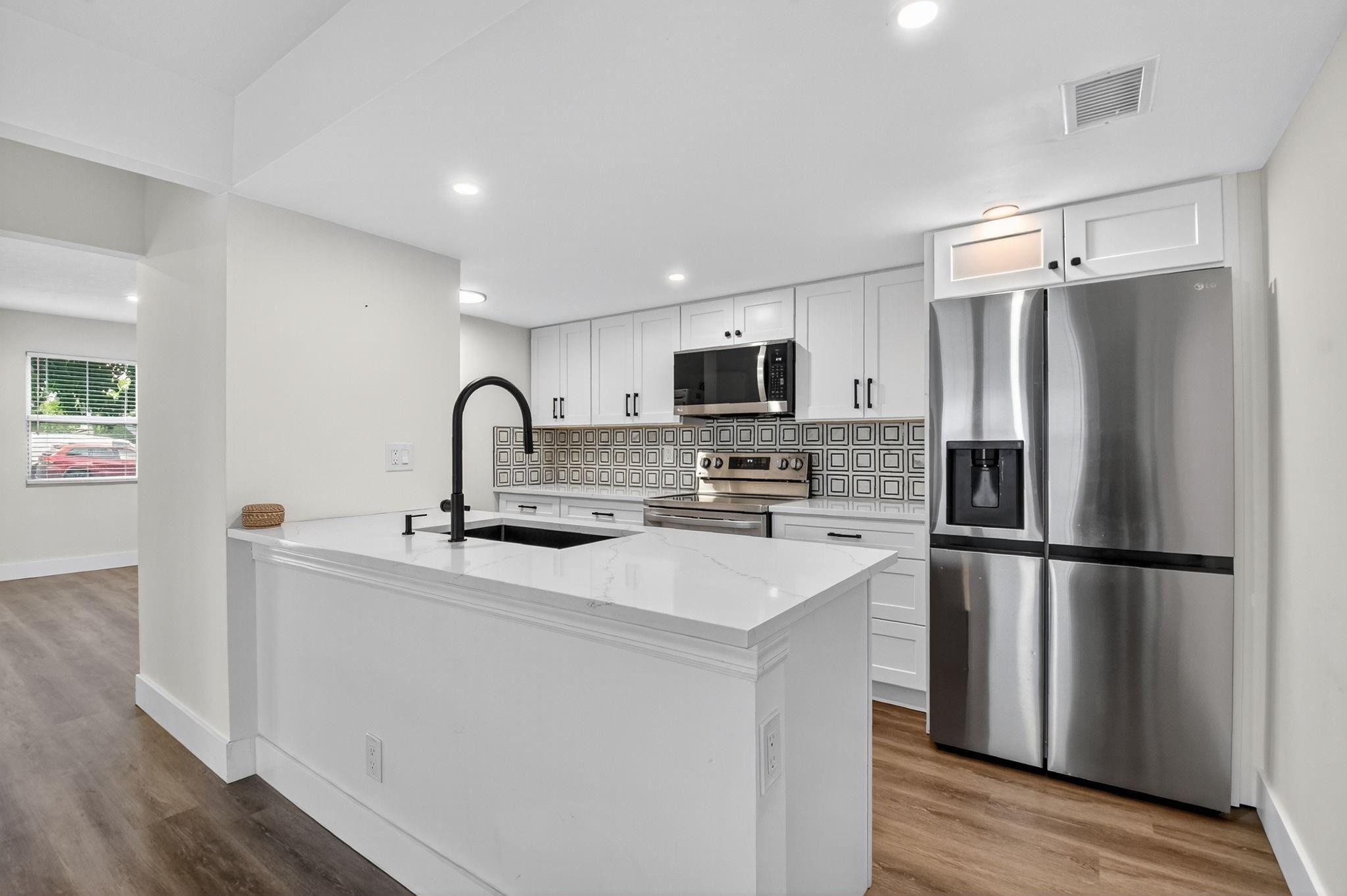 Kitchen with a large white island, stainless steel appliances, and geometric patterned backsplash.