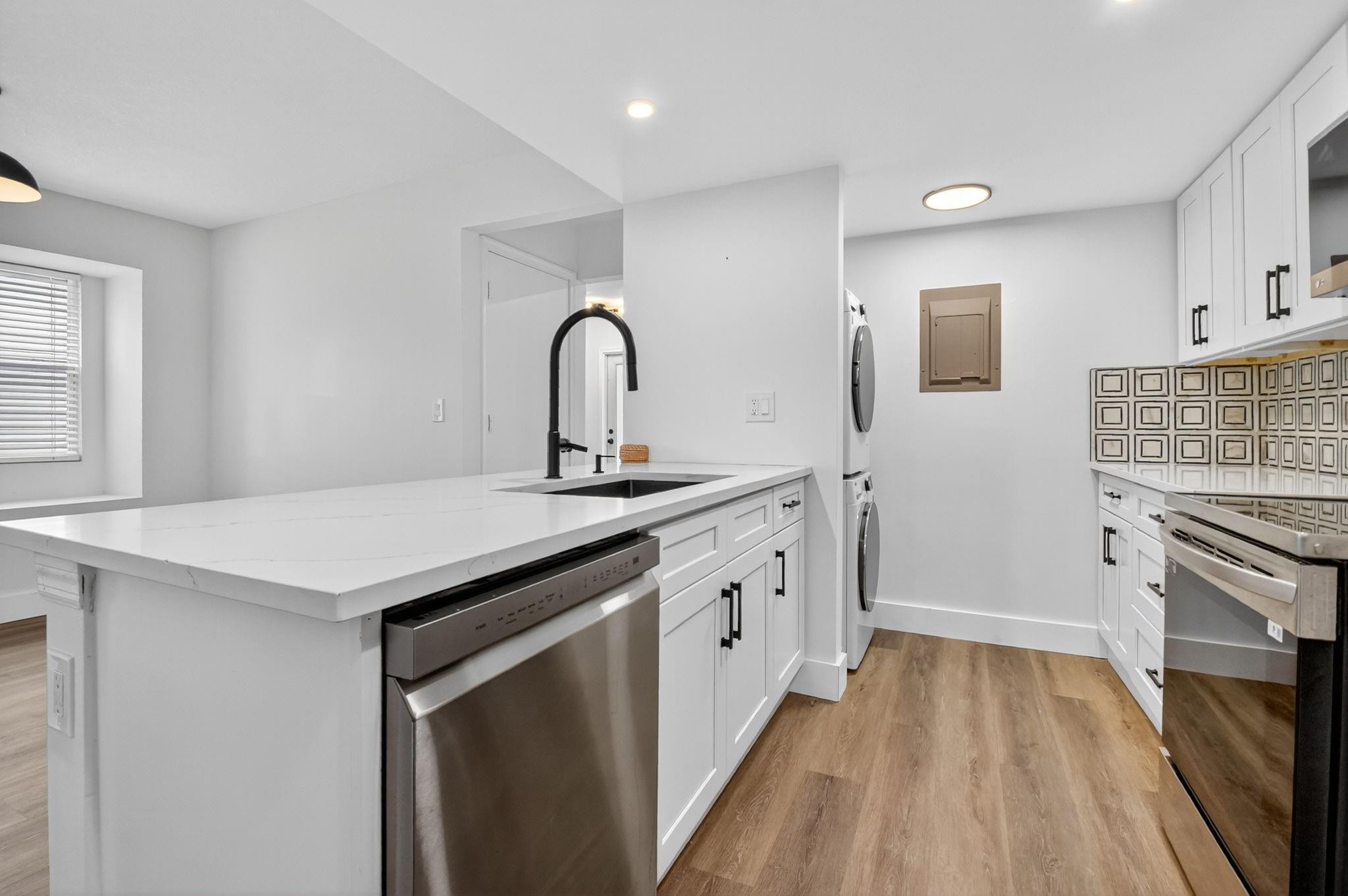 Kitchen with white cabinets and countertops, stainless appliances, patterned backsplash, and wood-look flooring.