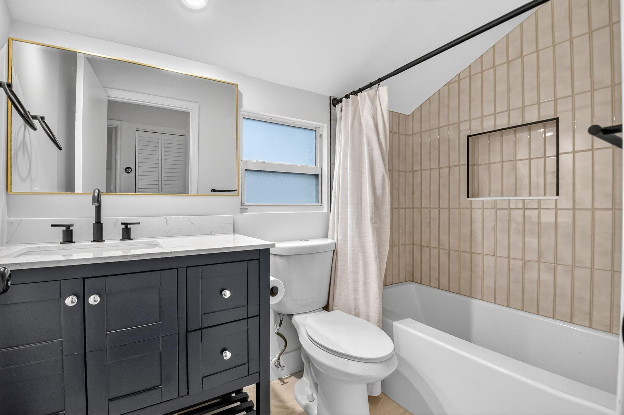Bathroom with a dark vanity, marble-look countertop, and bathtub with beige tiled surround.