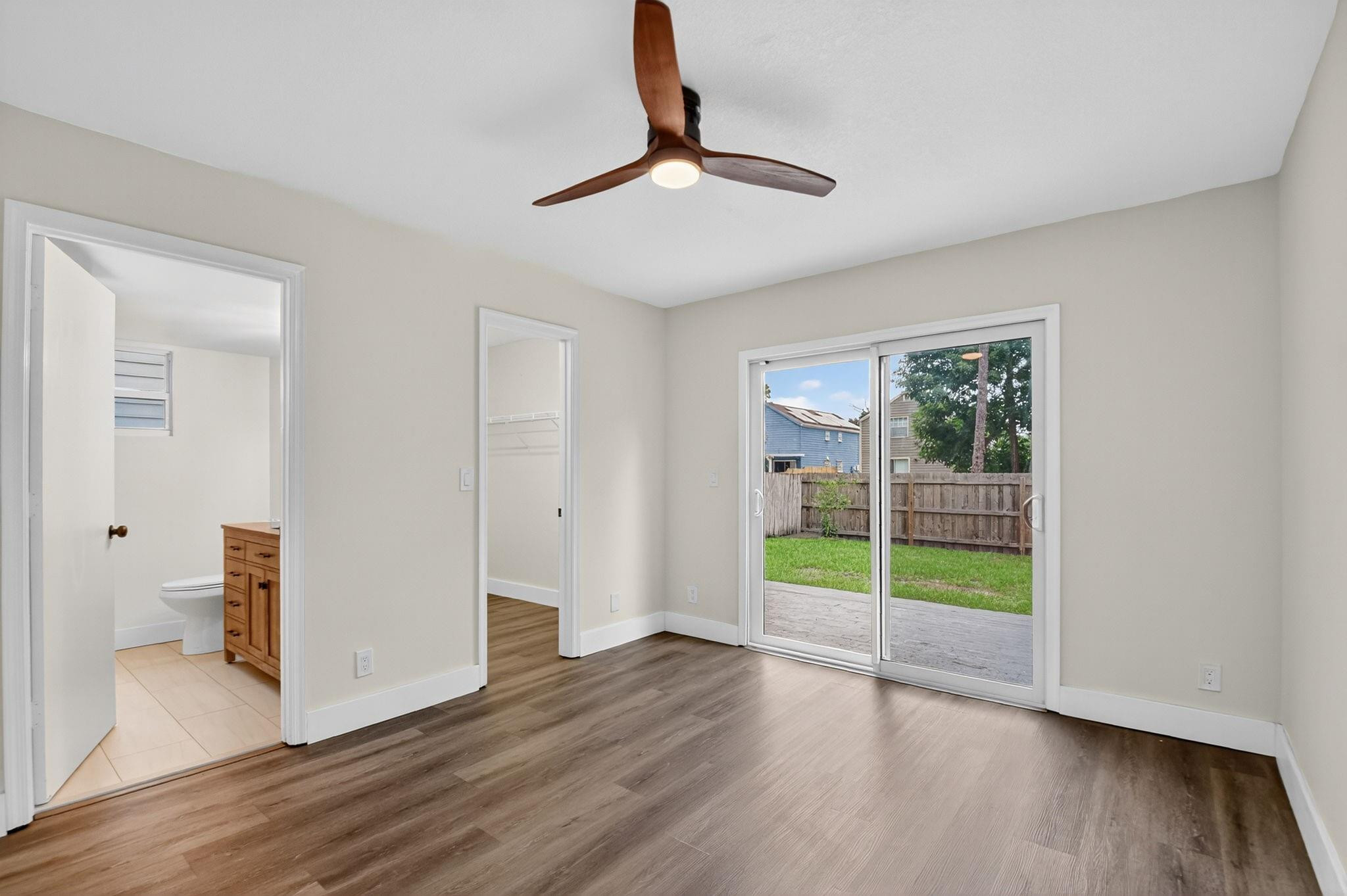 Empty bedroom with a ceiling fan, closet, and sliding glass doors to a fenced backyard.