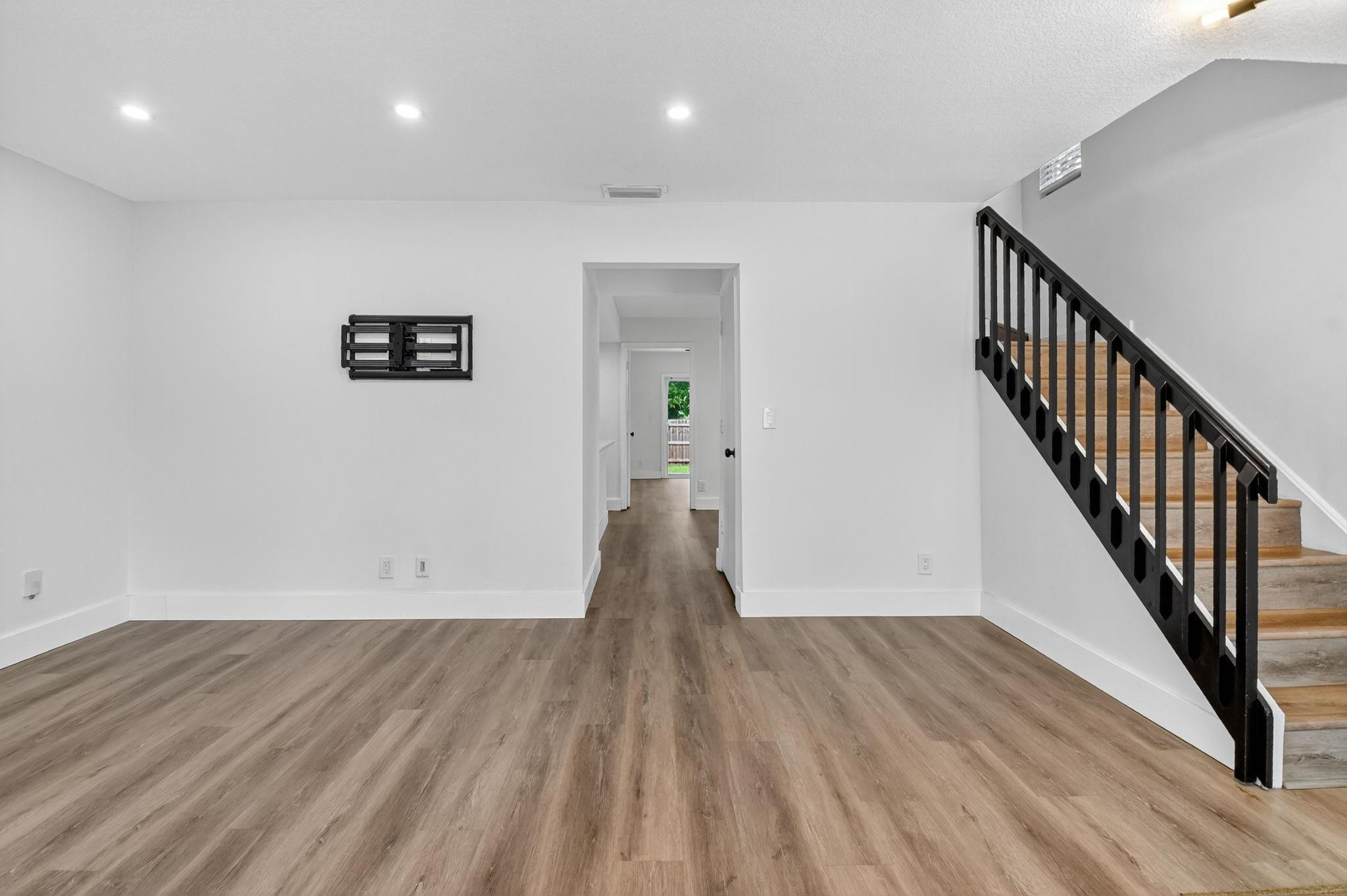 Empty room with wood-look floors and a staircase with black railings.