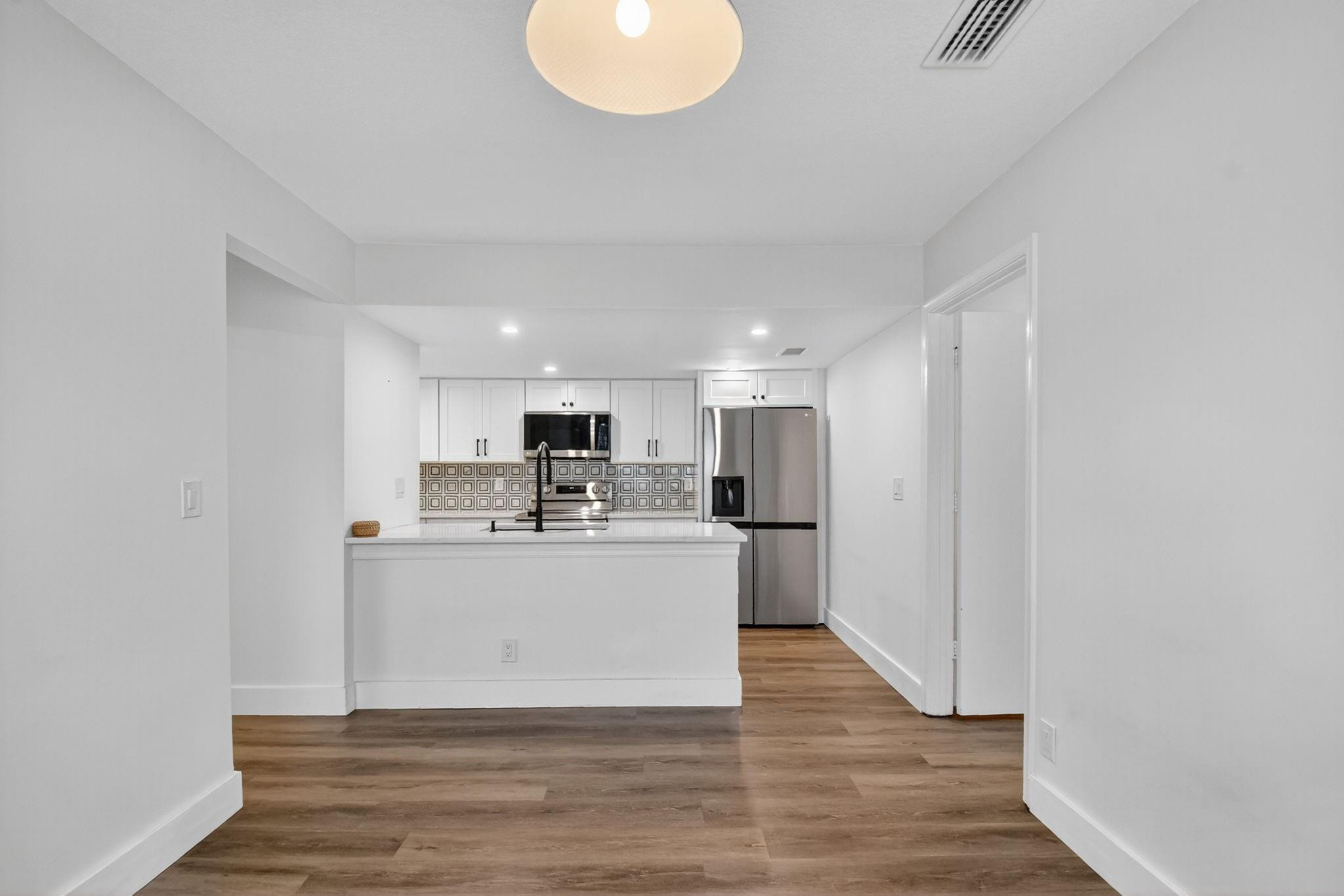 Kitchen with white cabinets, stainless steel appliances, geometric backsplash, and wood-look flooring.