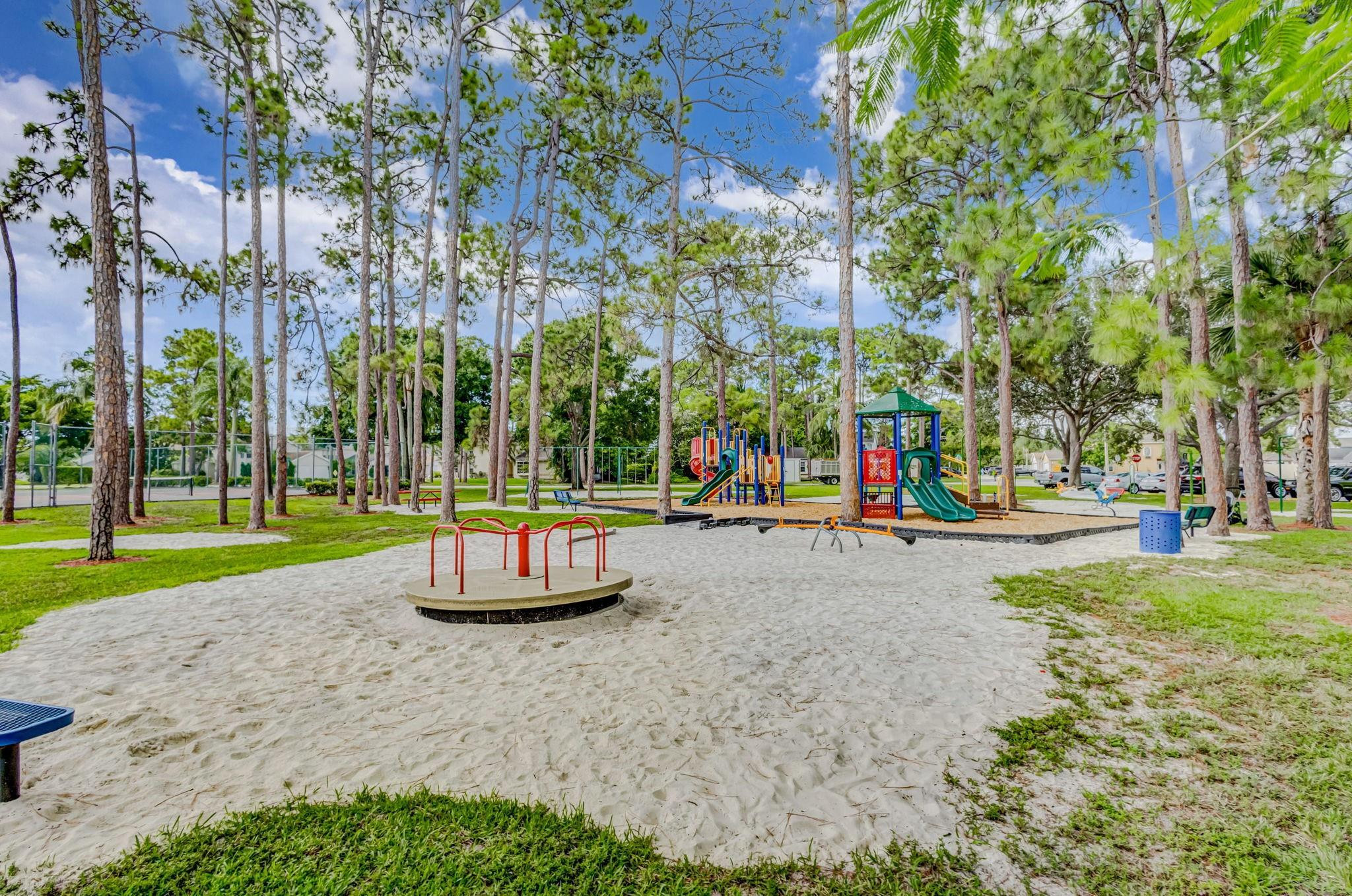 Community playground with colorful slides and climbing structures among tall pine trees.